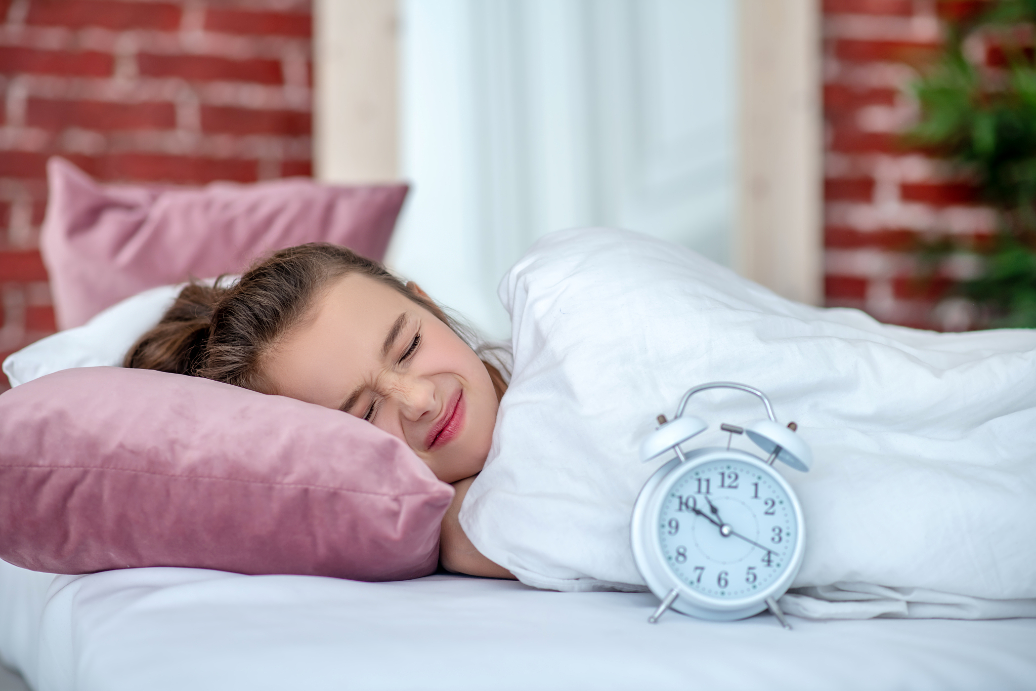 girl sleeping in white bed, next to white alarm clock.