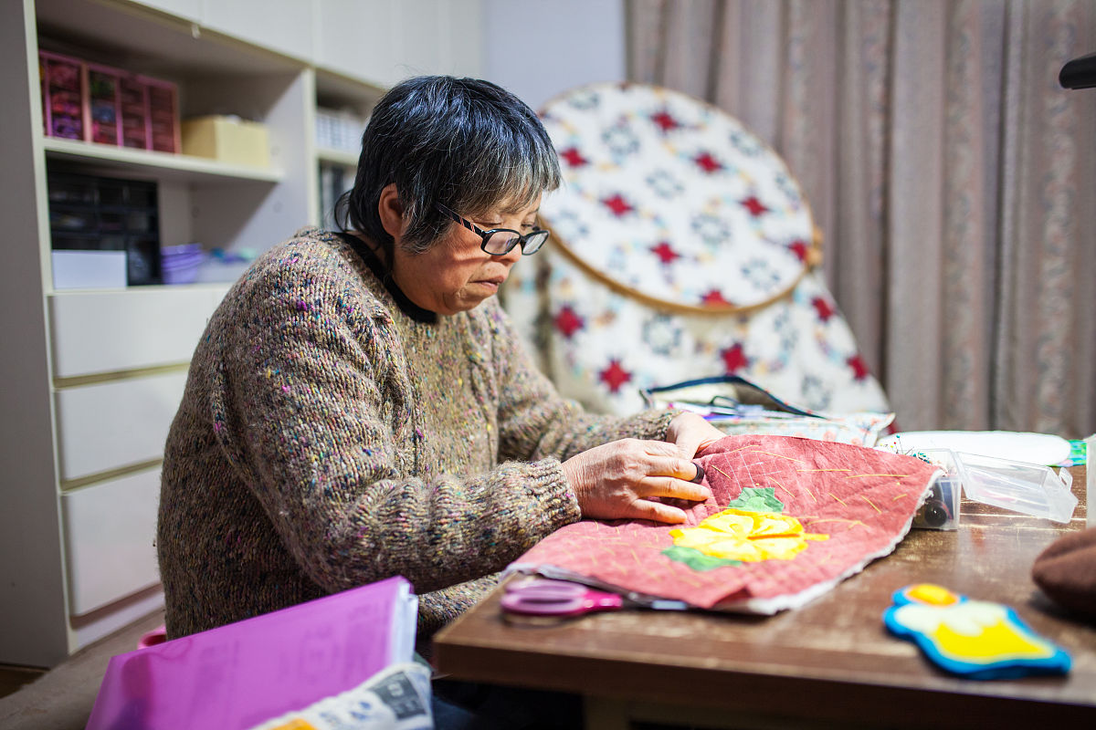 一位年长妇女在她的家中缝纫和制作工艺品
