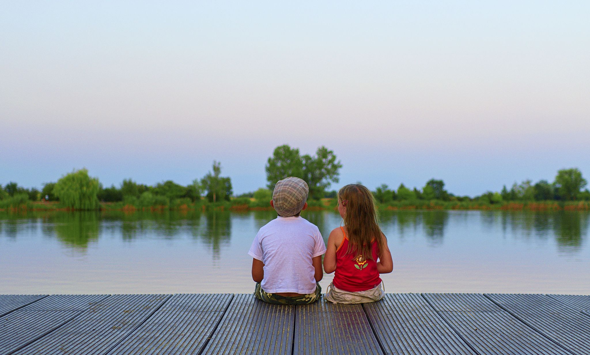 boy with flat cap and little girl are sitting on pier. boy and g