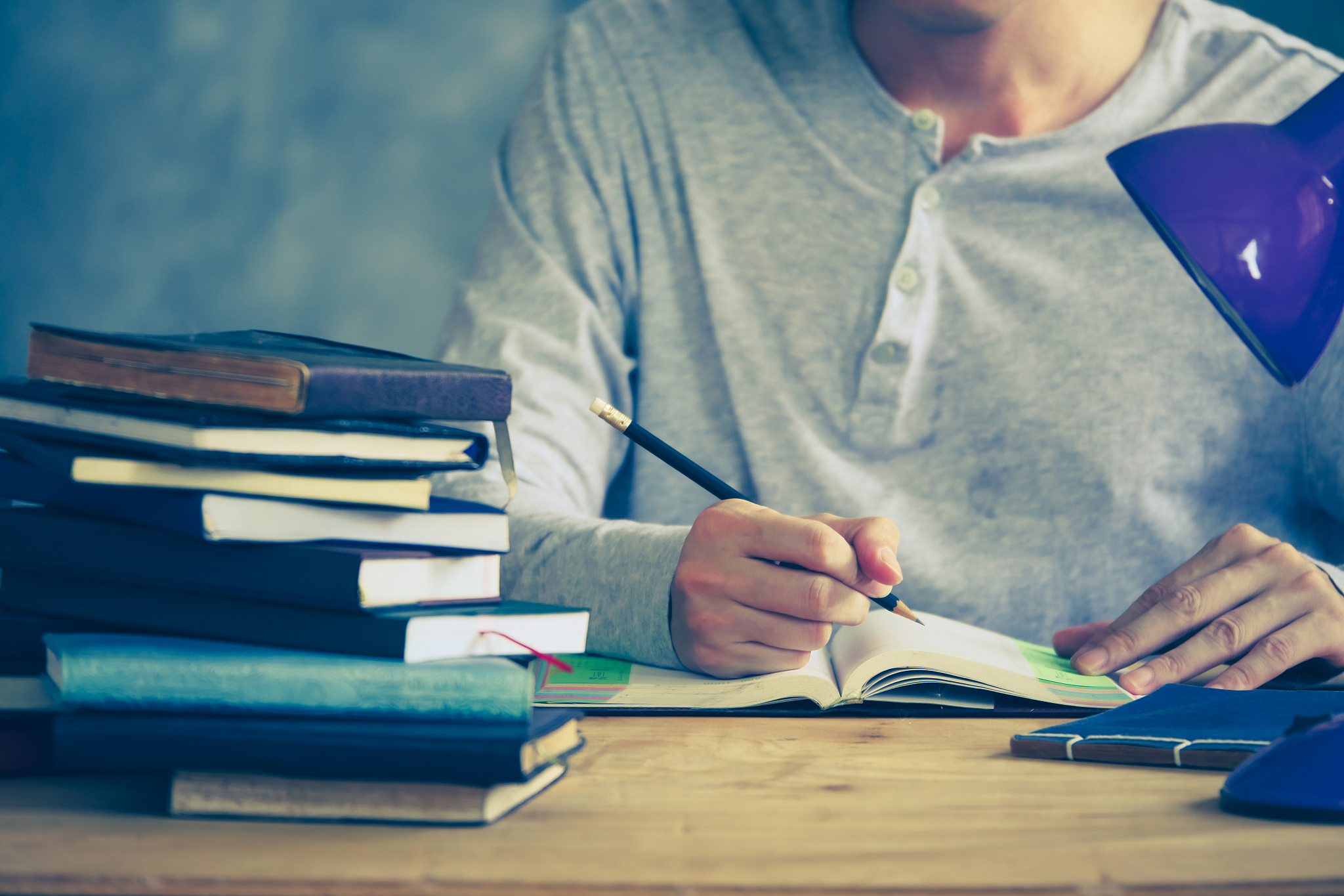 close up of a man writing in notebook, stack of old books on woo