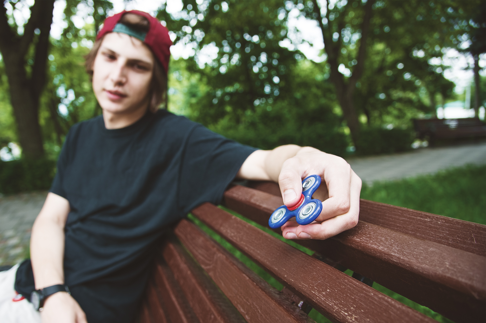 a long-haired hipster in a cap sits on a bench and spins a fidge