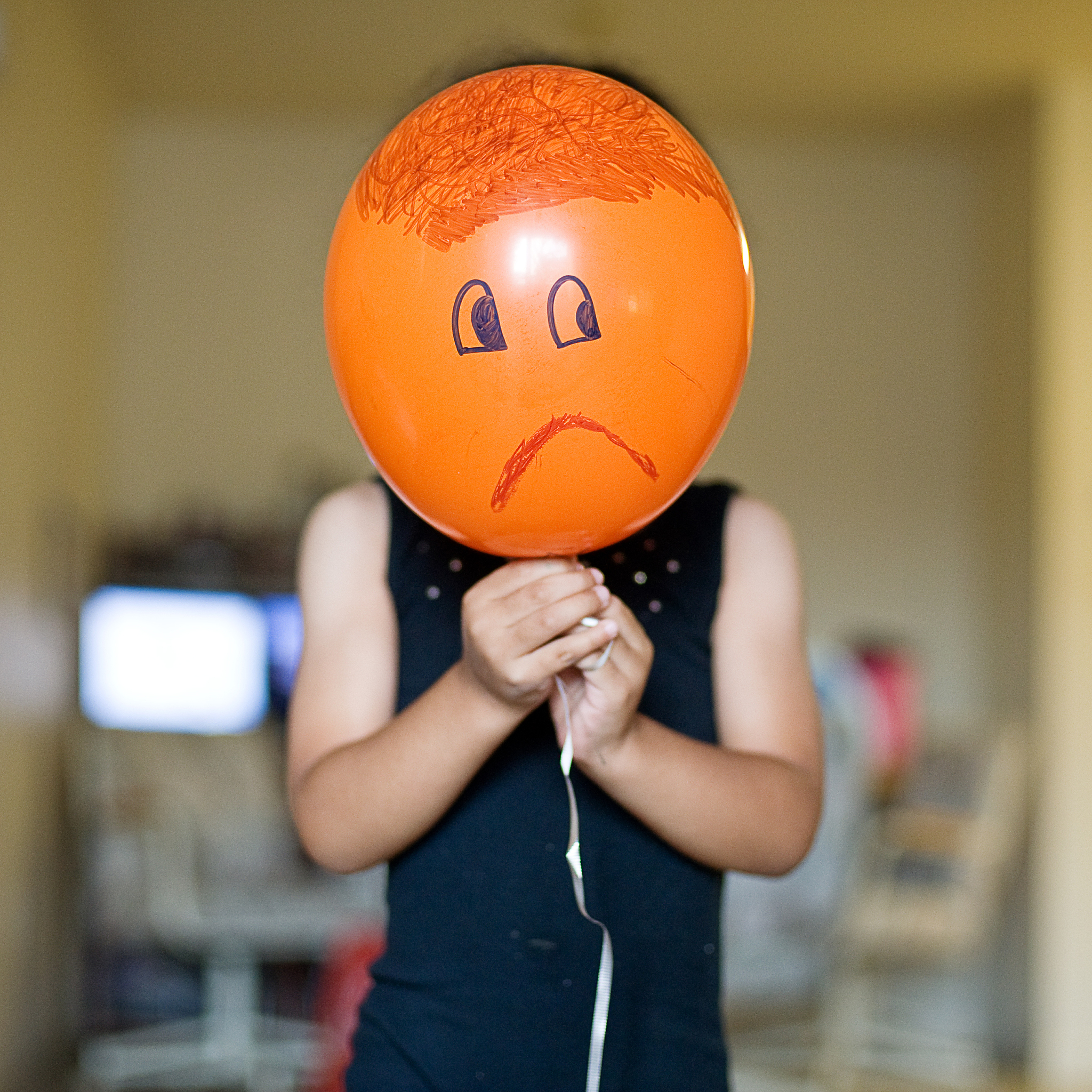 child holding an orange balloon with sad face