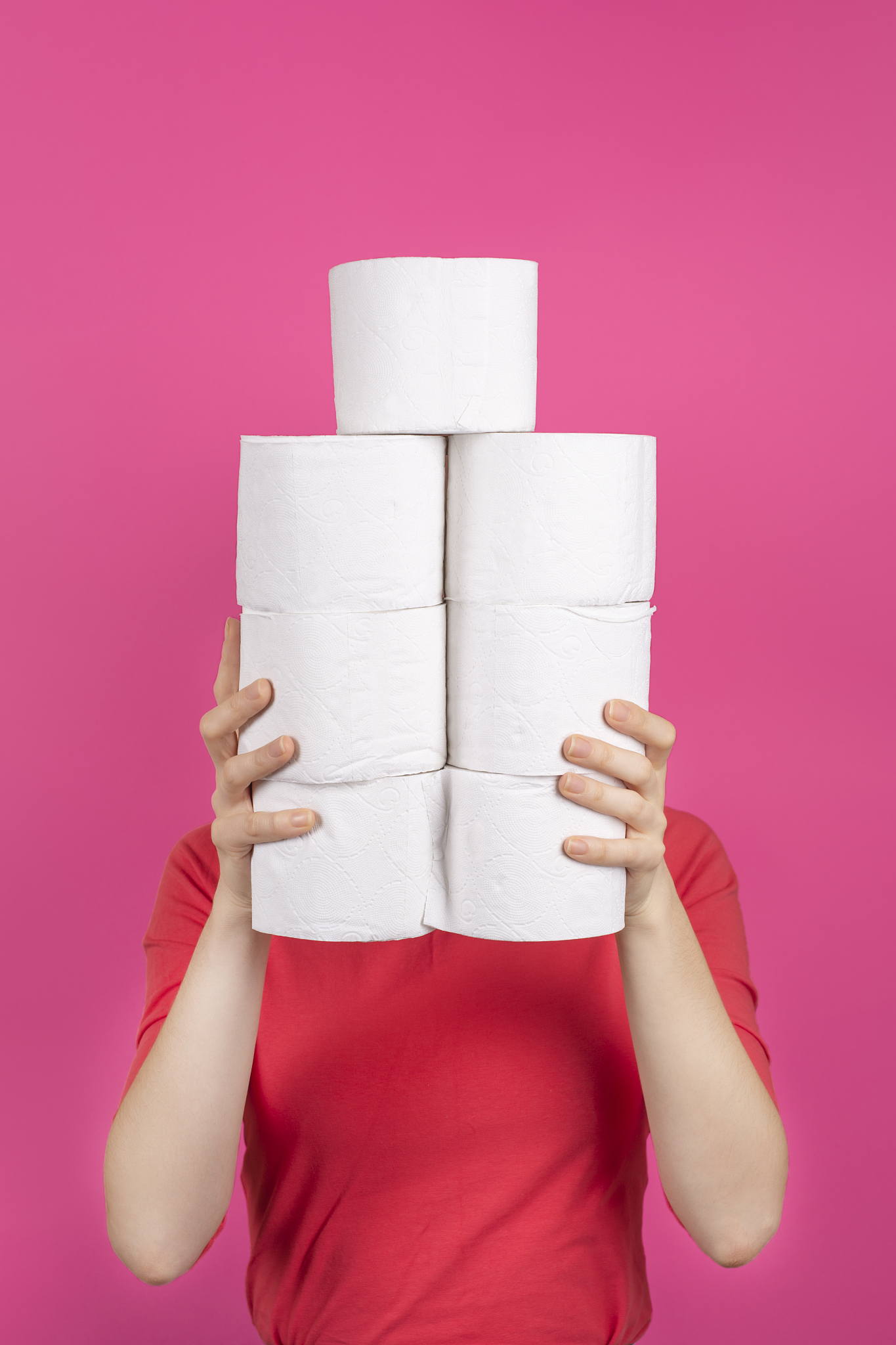 young woman holds big stack of toilet paper rolls.