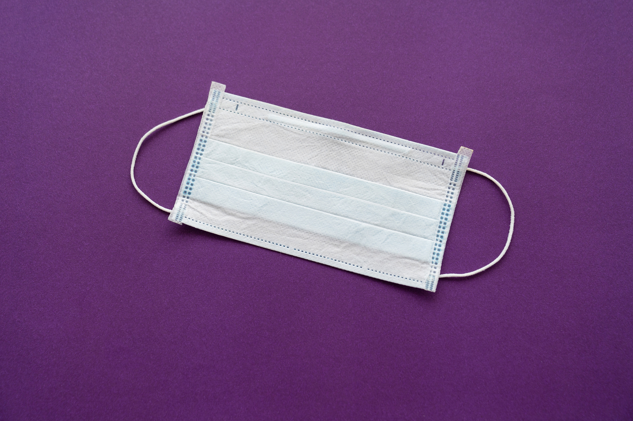 a disposable medical mask on a purple background.