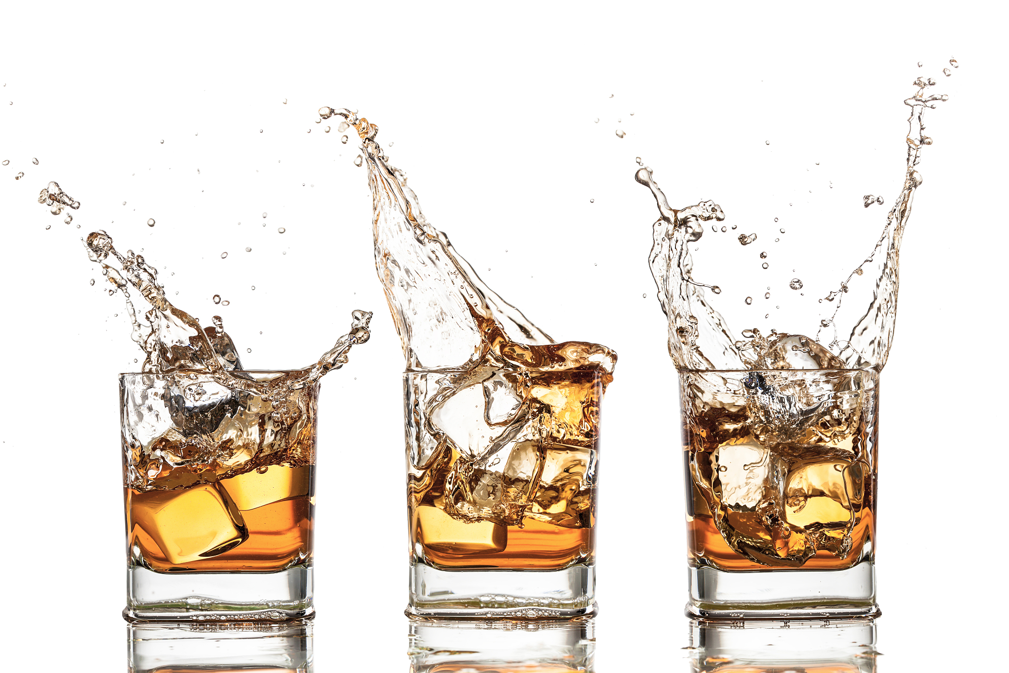 three glasses of whiskey being splashed by ice cubes