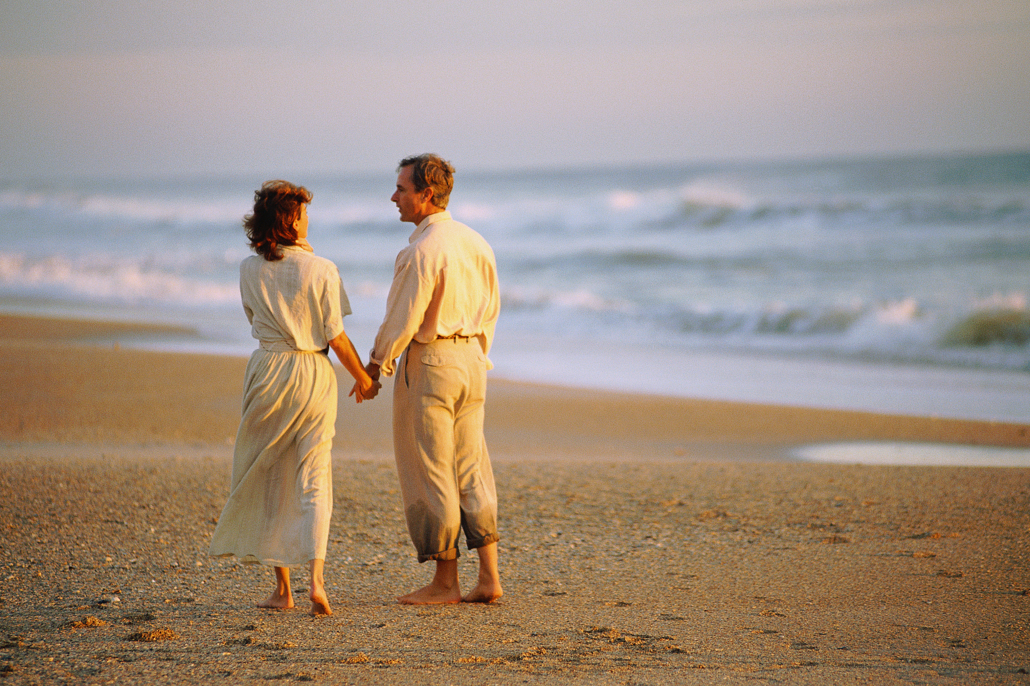 man and woman holding hands  walking on beach