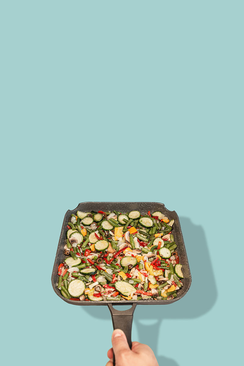封面与男人的手握一个方形陶瓷煎锅与地中海饮食蔬菜的混合,孤立与阴