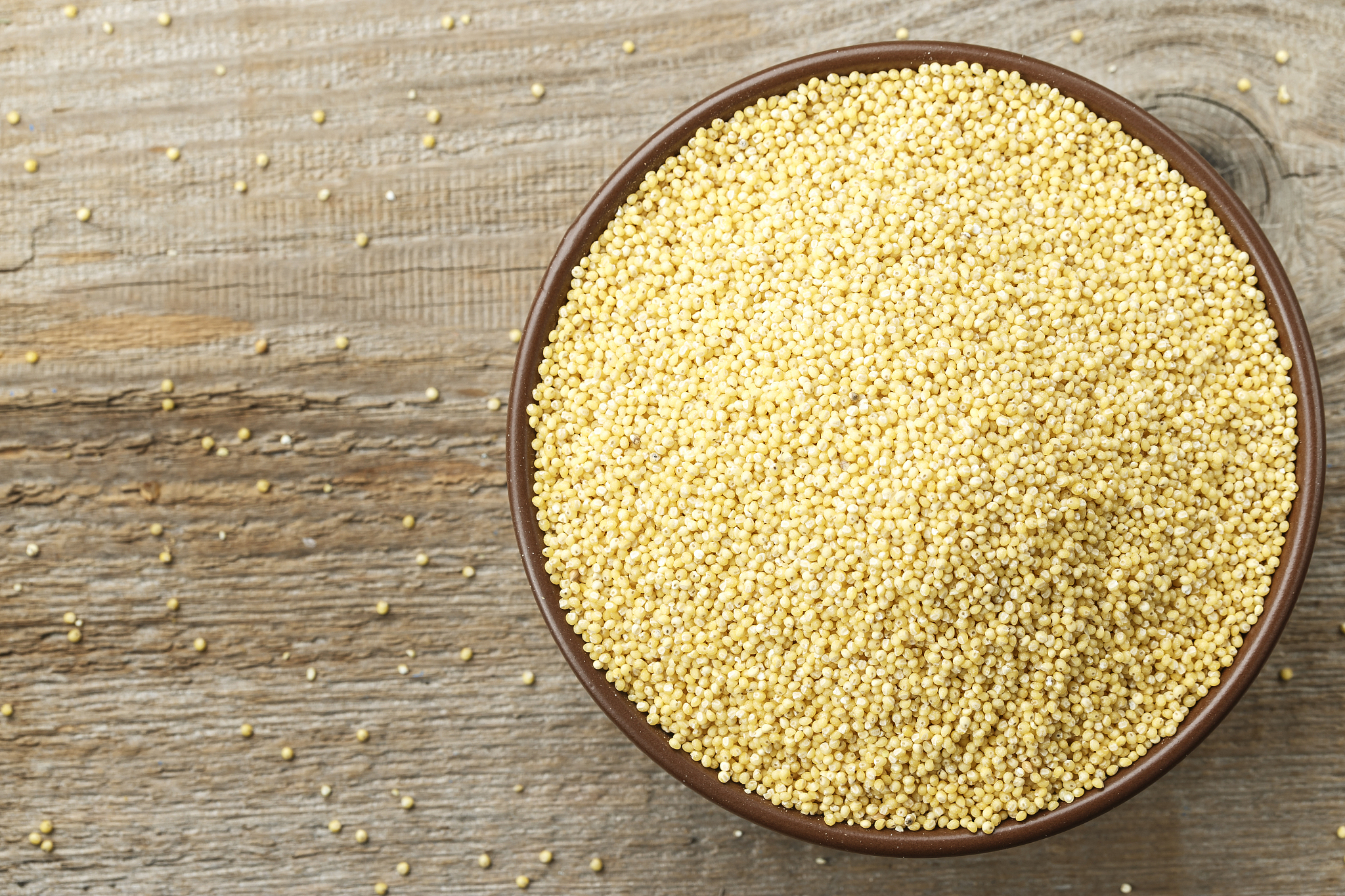 raw millet grains in a clay plate on a wooden background, top vi