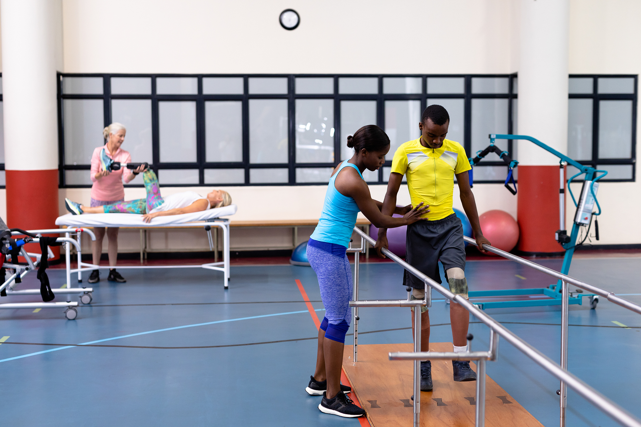 physiotherapist helping disabled man walk with parallel bars in 