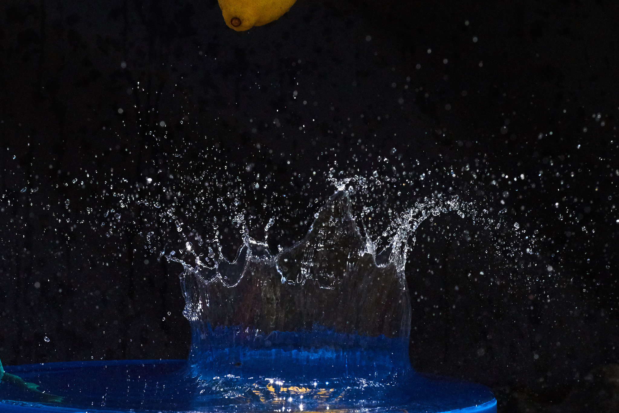 yellow lemon falling in the blue water on a black background