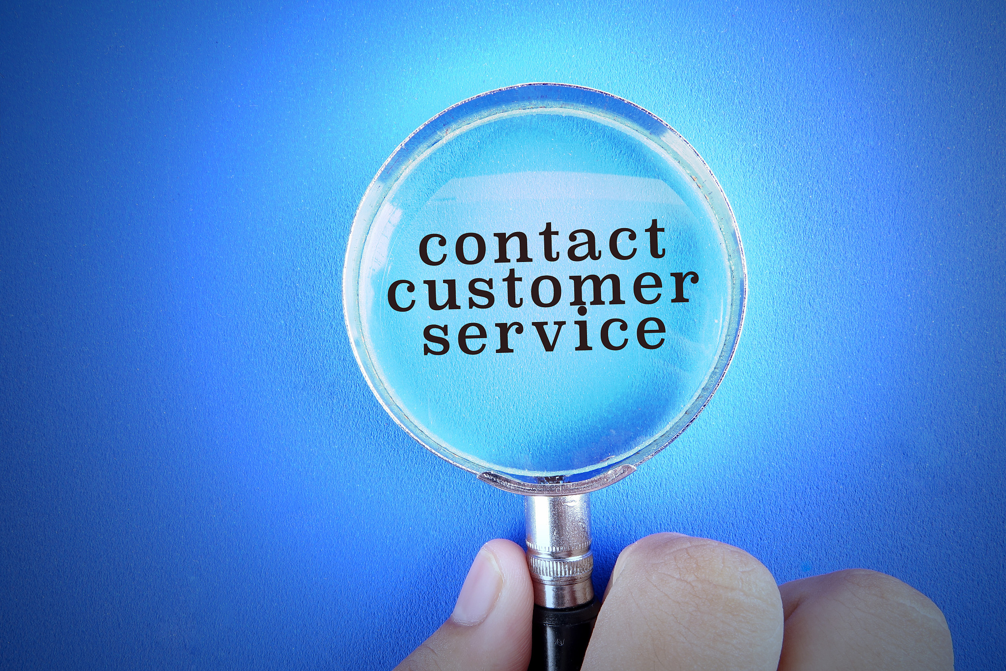 hand holding magnify glass over a blue background with contact c