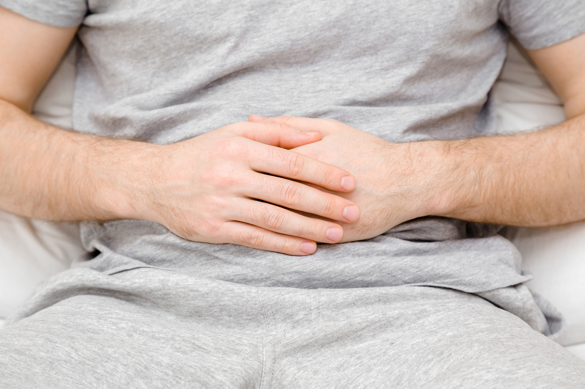 man sitting or lying down on bed. hands touching belly. sufferin