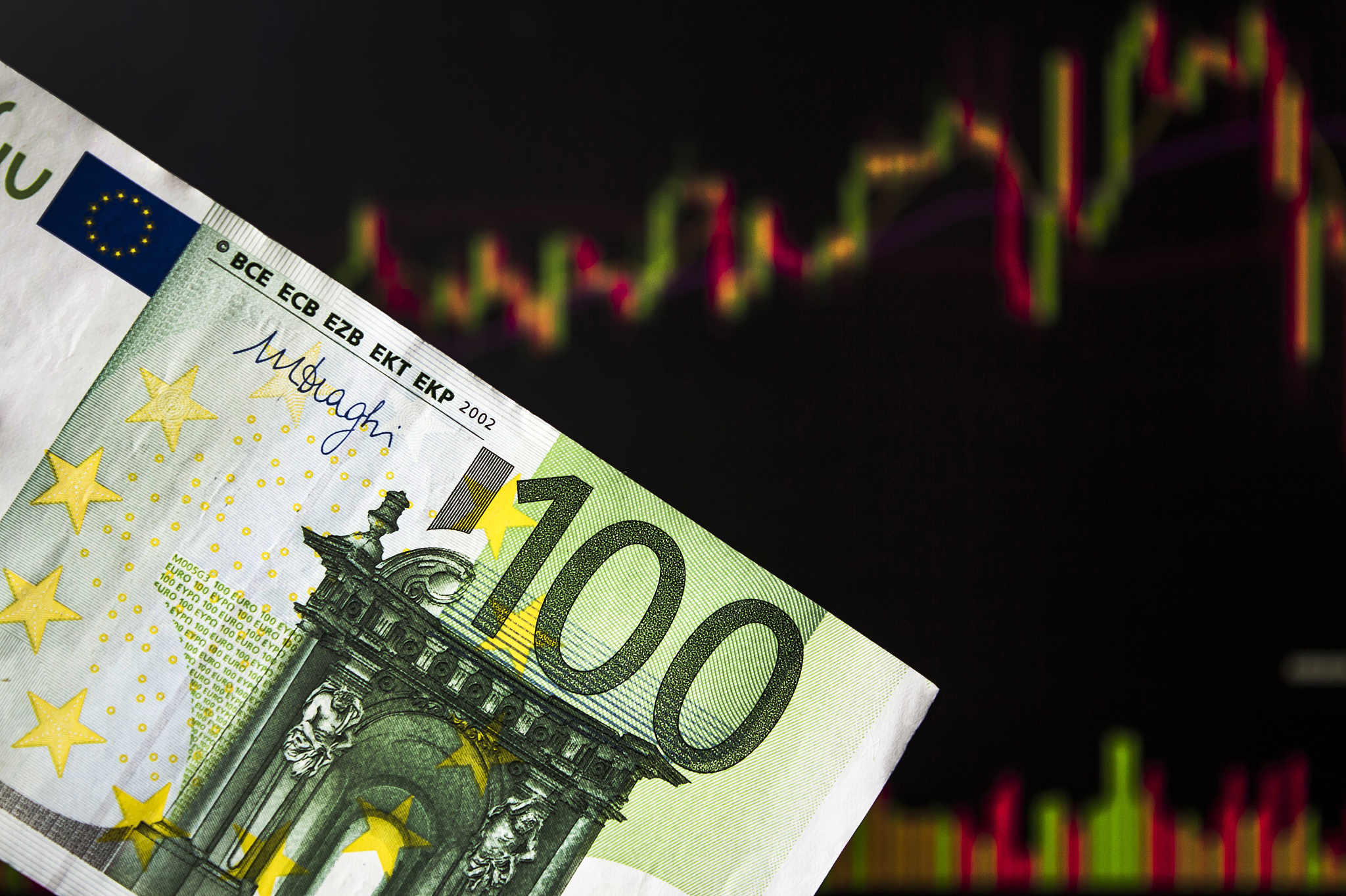 hands holding euro, eur in front of a laptop monitor with a pric