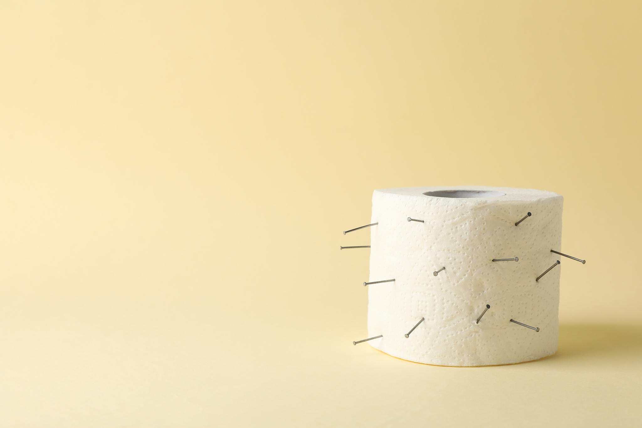 toilet paper with nails on beige background. hemorrhoids