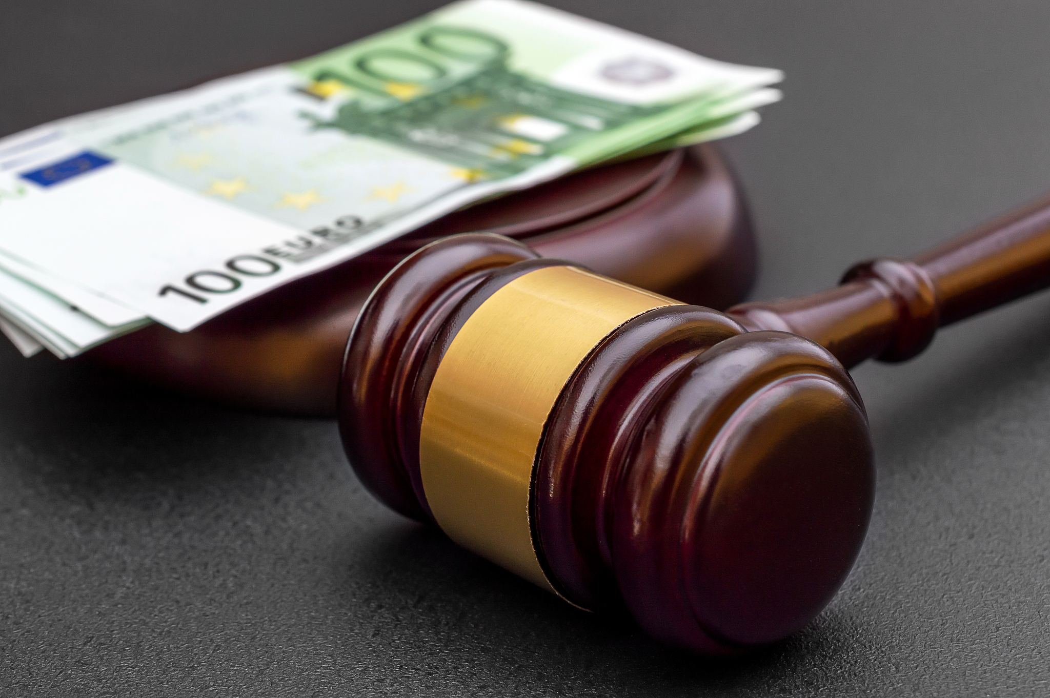 judge's gavel with one hundred euro banknotes on black.