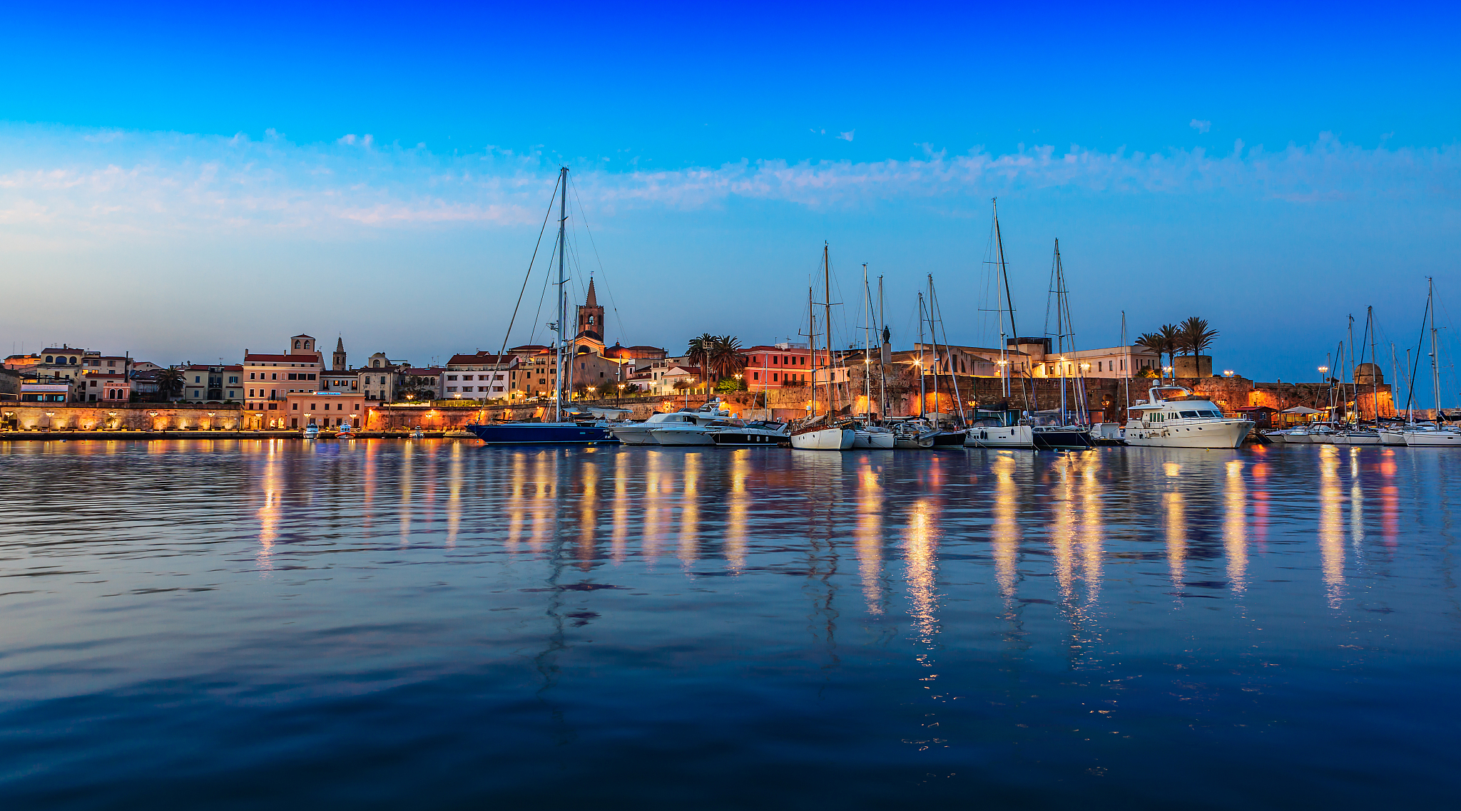 sailboats moored on sea by buildings against blue sky