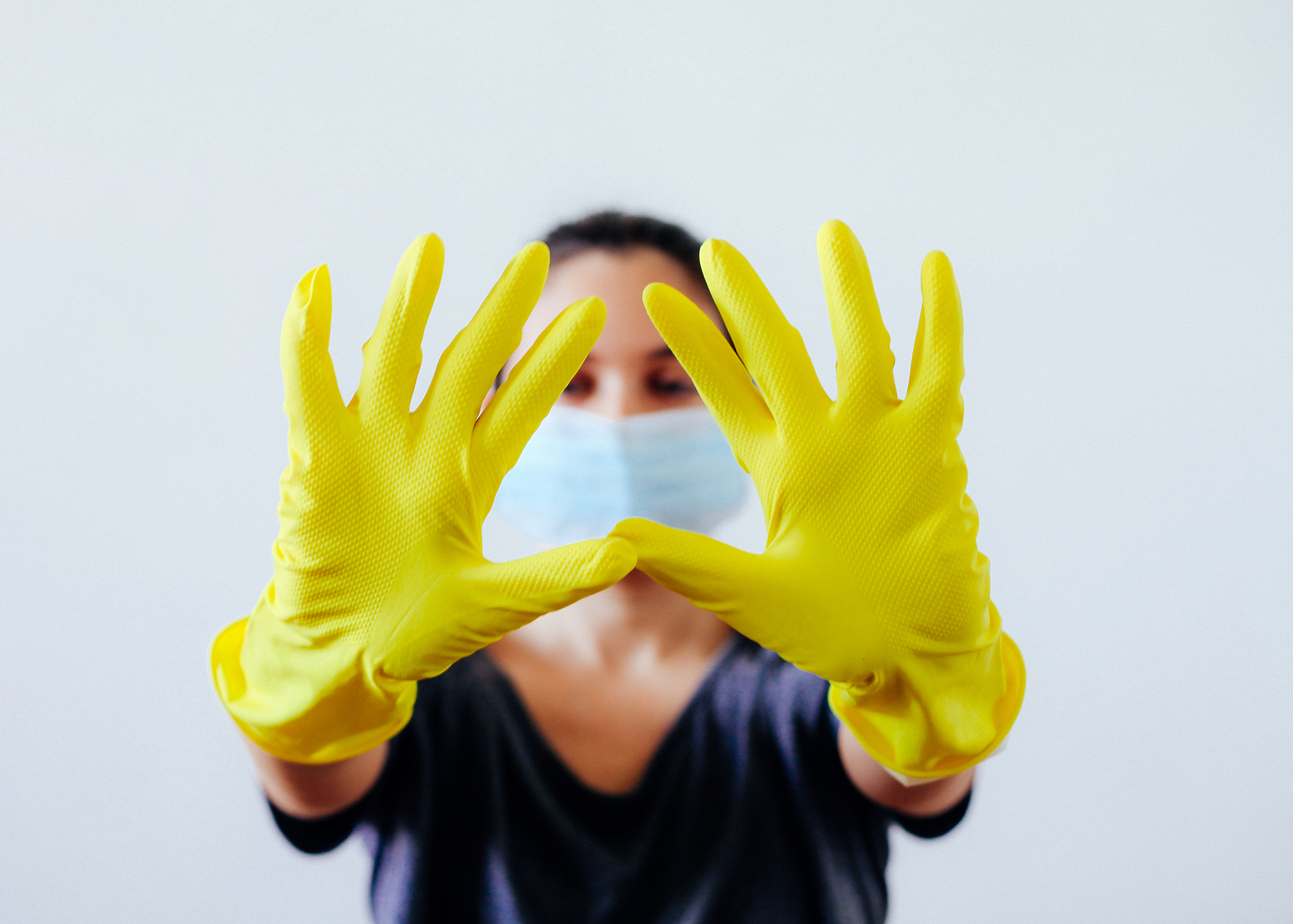 young woman hiding her face with yellow protective rubber gloves