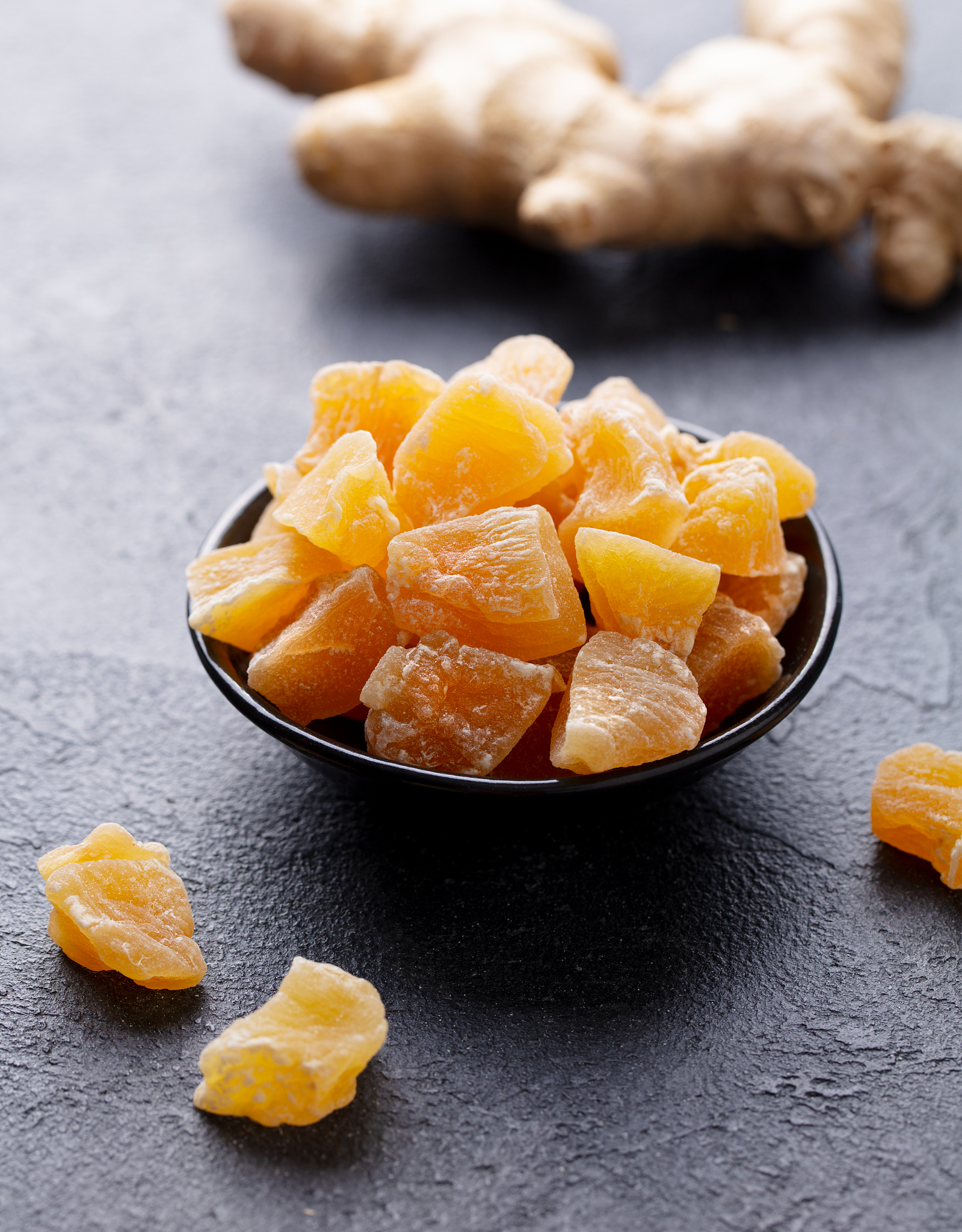 candied ginger in black bowl on dark stone background. close up.