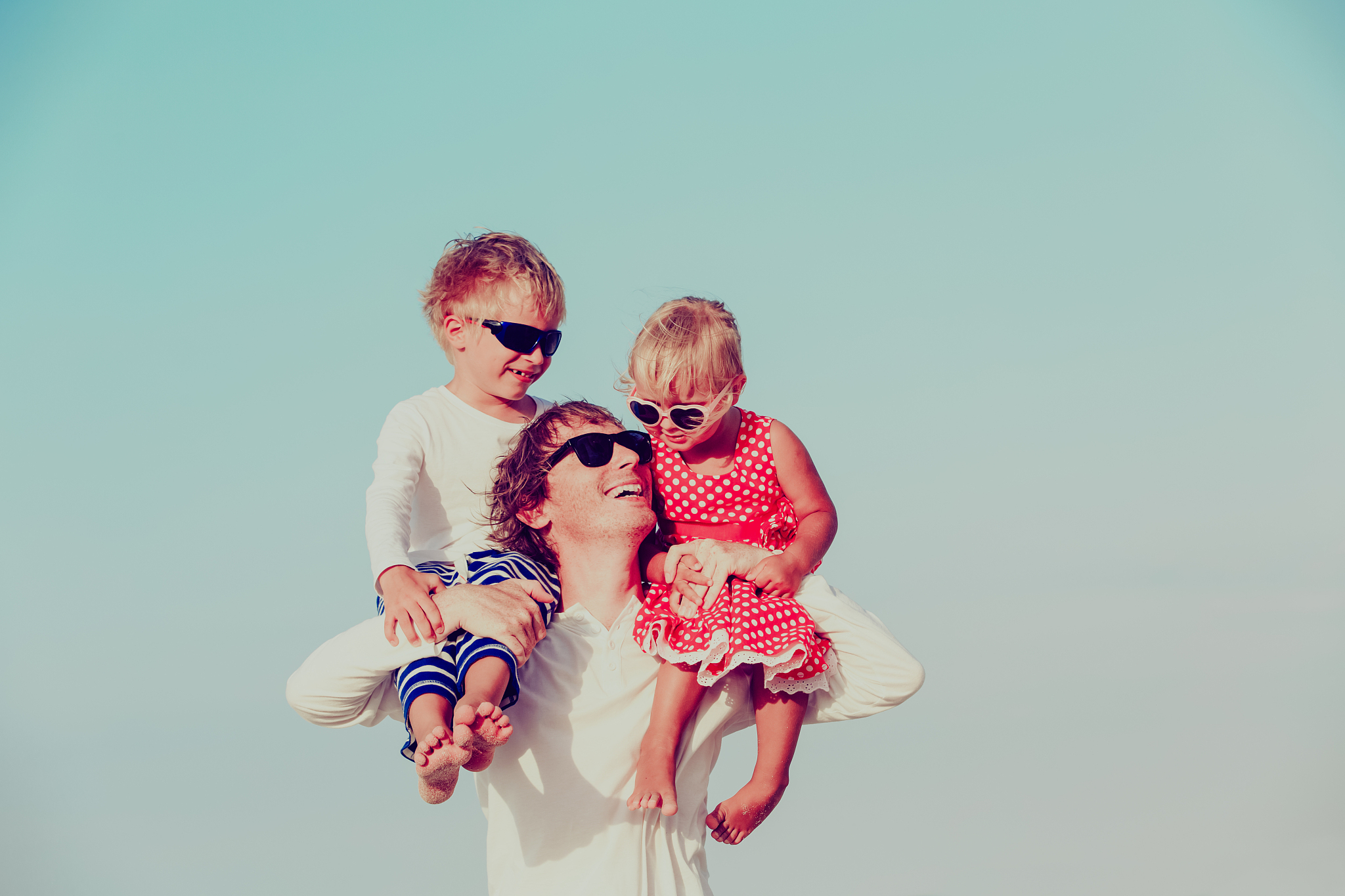 happy father with two kids on shoulders at sky