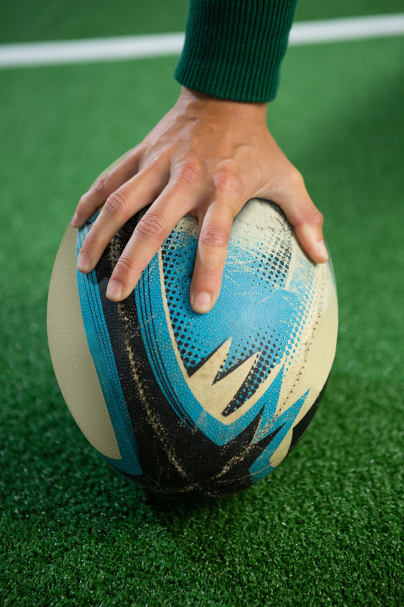 close up of hand holding rugby ball on field