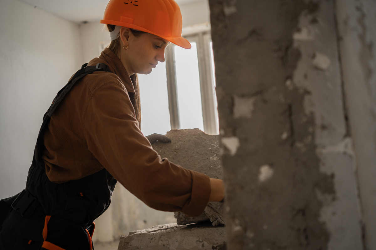 女建筑工戴着安全帽在户外建筑工地搬运沉重的混凝土板