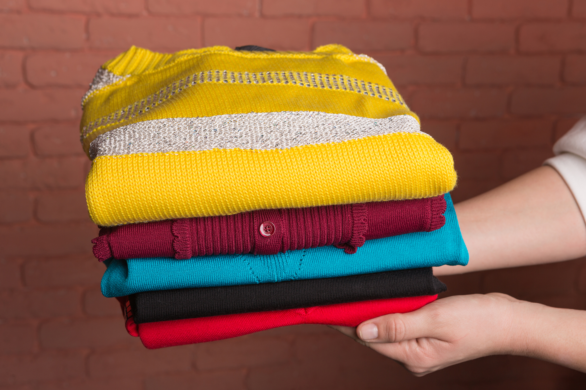 women's hands hold a stack of folded colored women's sweaters, a