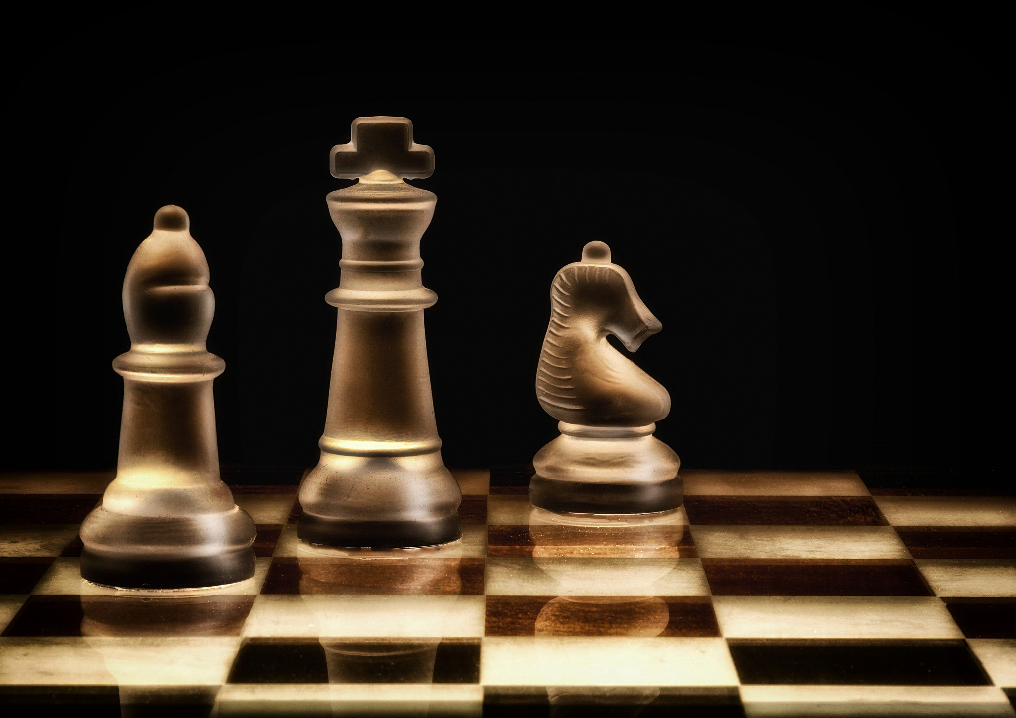 three glass chess pieces on a glass chess board