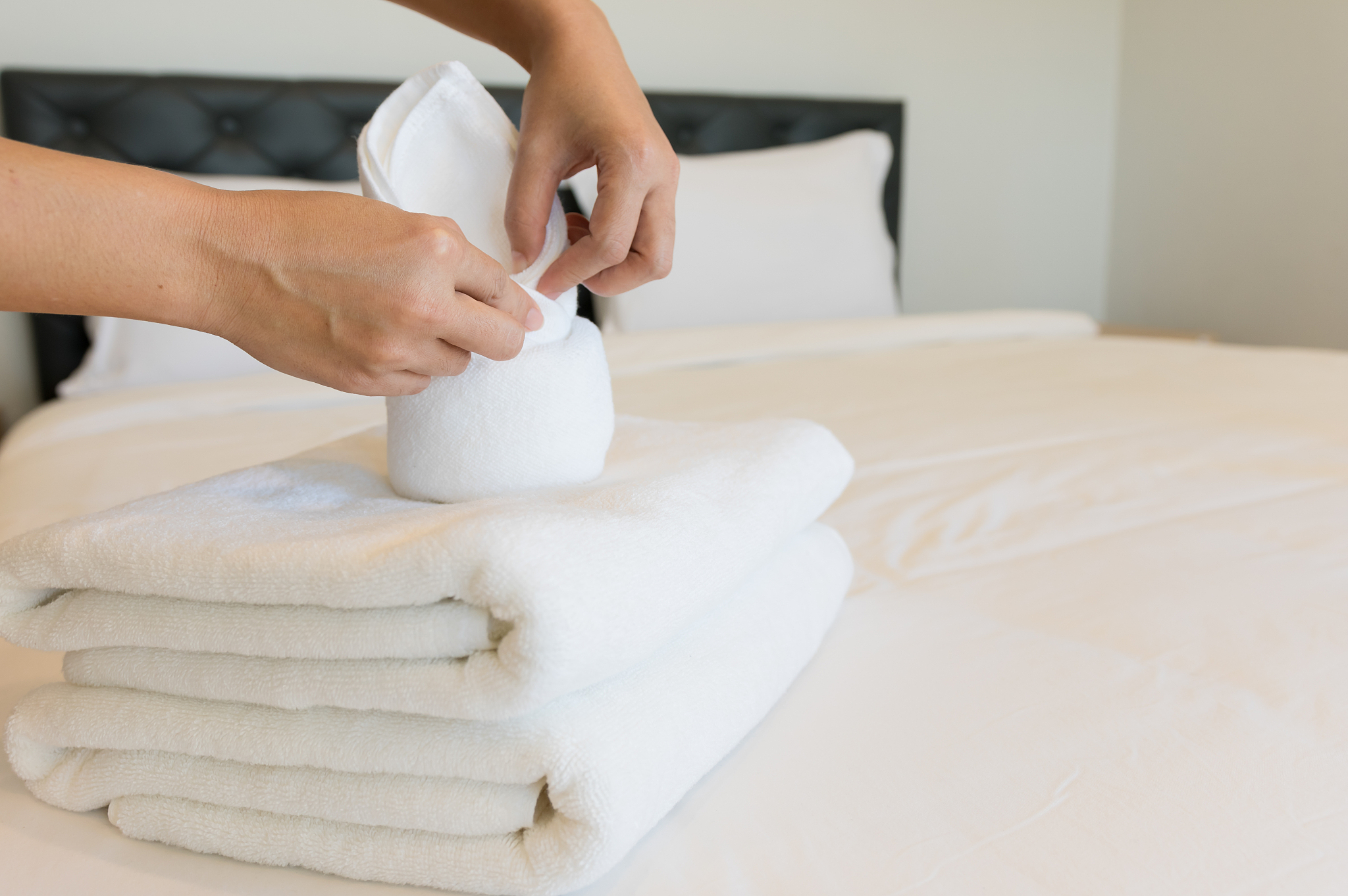 cropped hands of woman folding towel on bed