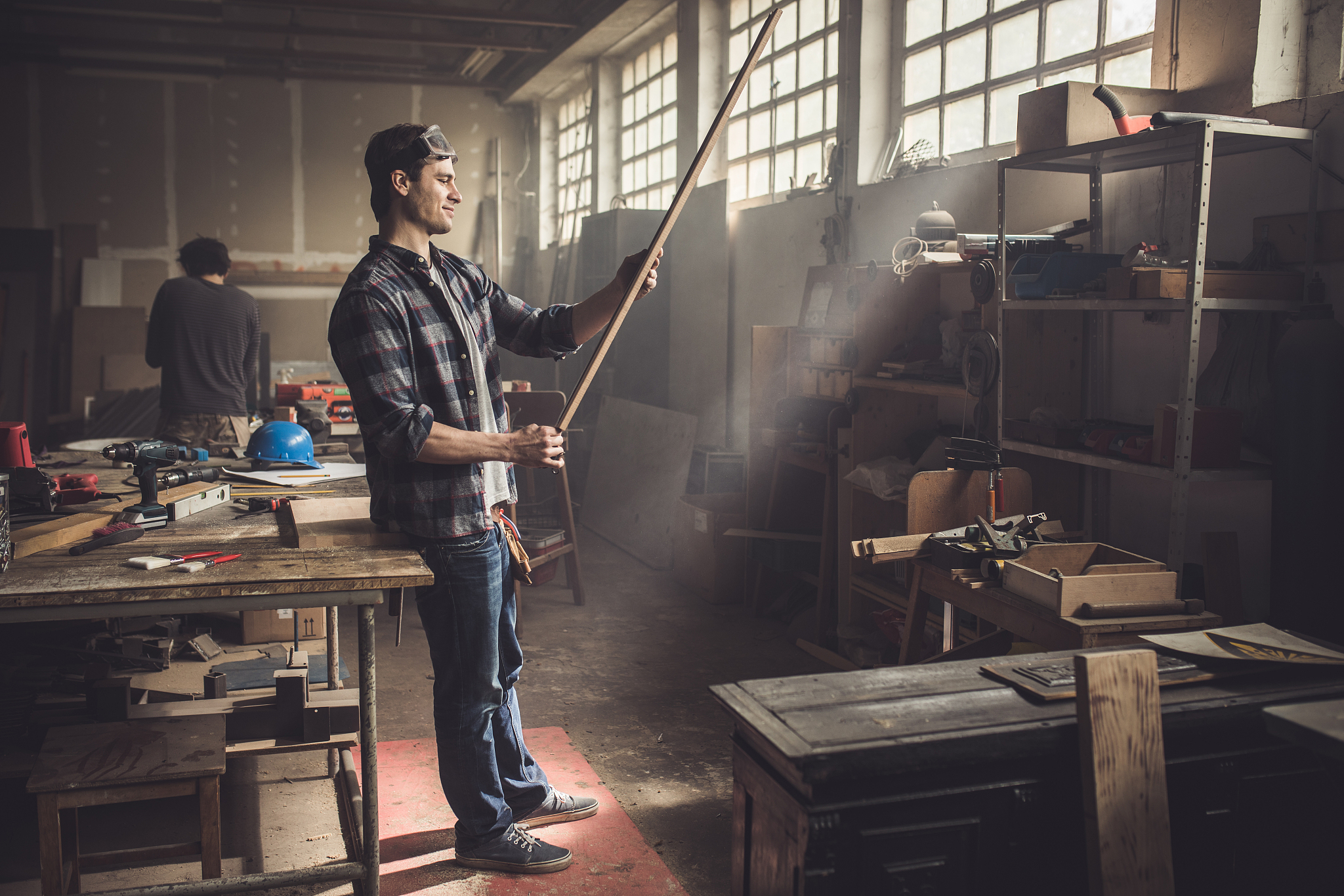smiling carpenter measuring wood plank in a workshop.