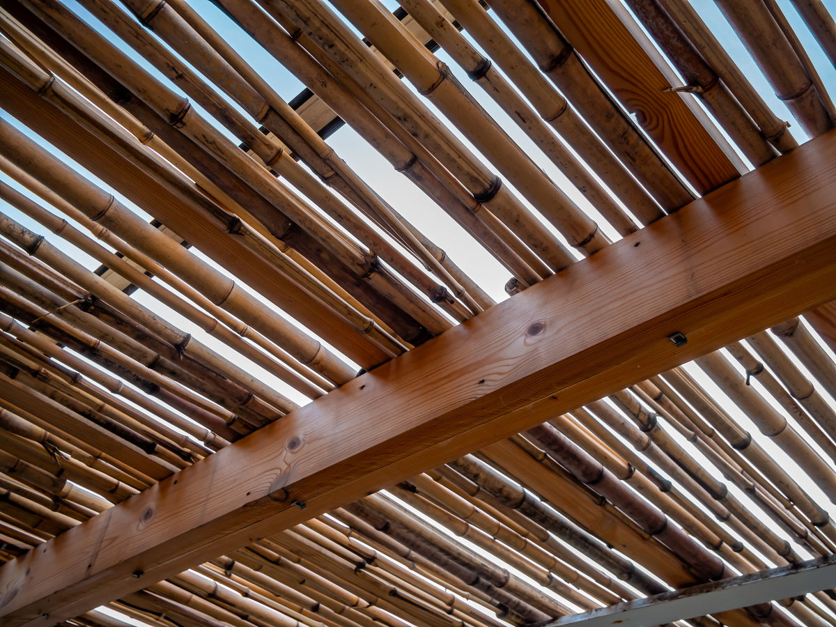 请将这段话屋顶是竹框架结构 层竹梁分别依垂直和对角线方向排布在恰当的角度；建筑的短边方向和楼梯都特别进行了加固支撑梁上下两端再加入构造绑扎起来框架上表面再附加风撑；在竹框架中间架设一排竹椽支撑铁质波纹板屋面并覆盖木镶板调整到足够使用的高度用另种方式描述可以改变语序使用修辞手法