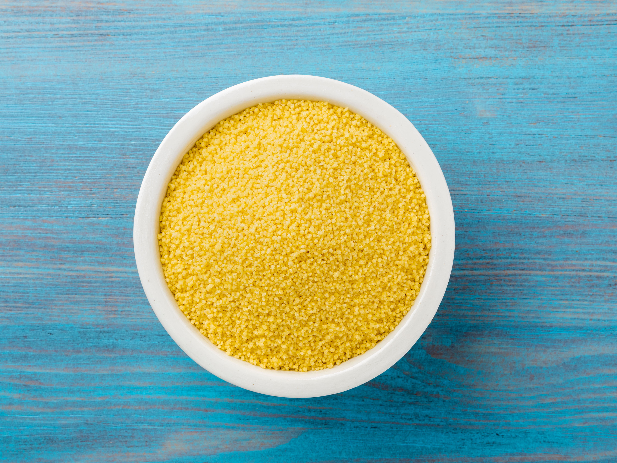 white bowl  with raw couscous on blue wooden background, top vie