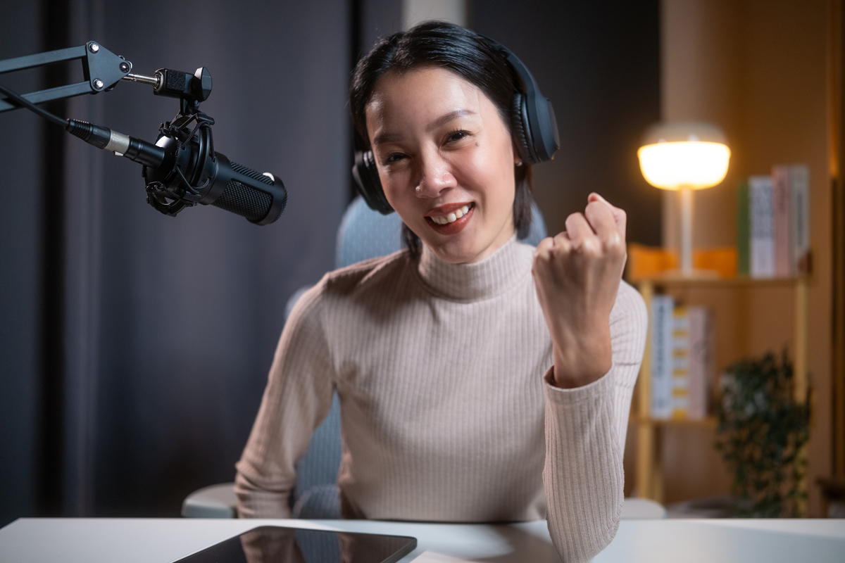 笑容灿烂的亚洲美女播客,戴着耳机,举起拳头庆祝,在的