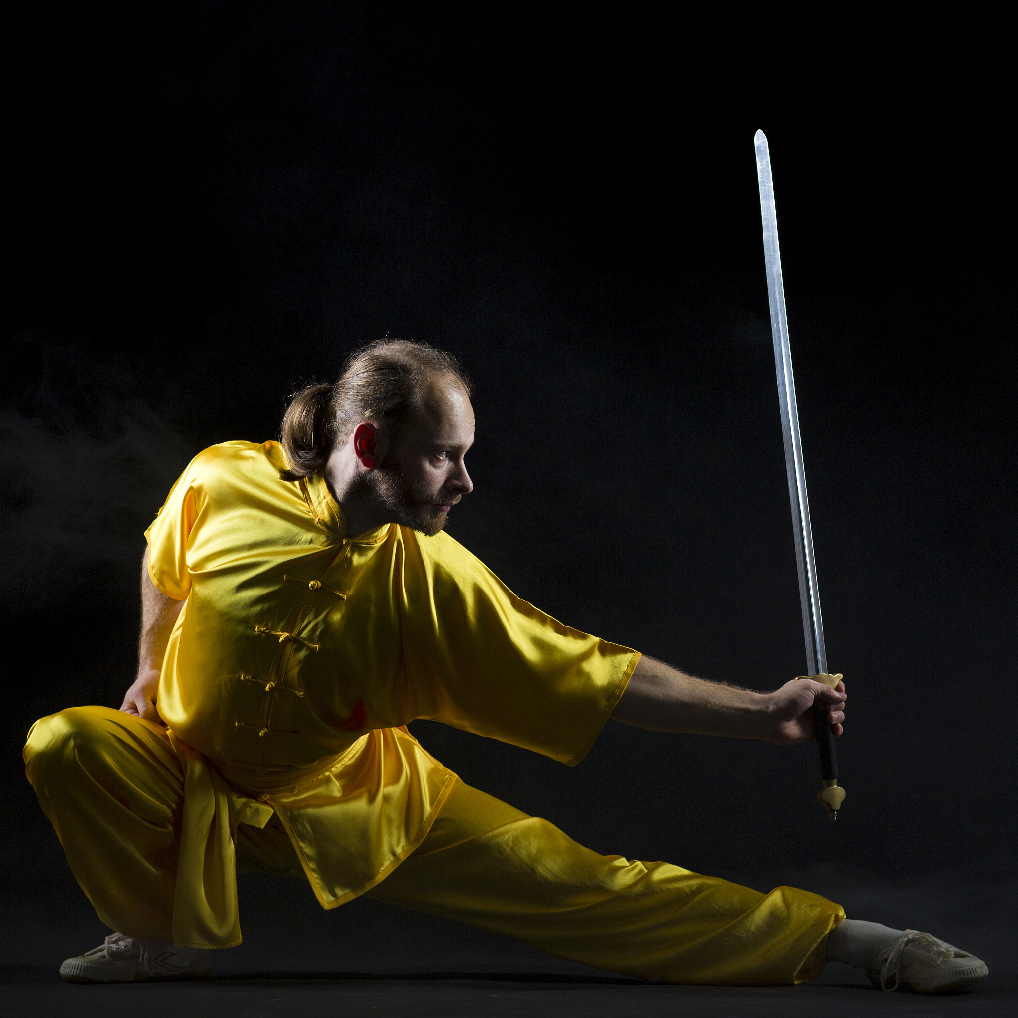 wushu fighting position with metal sword on black background
