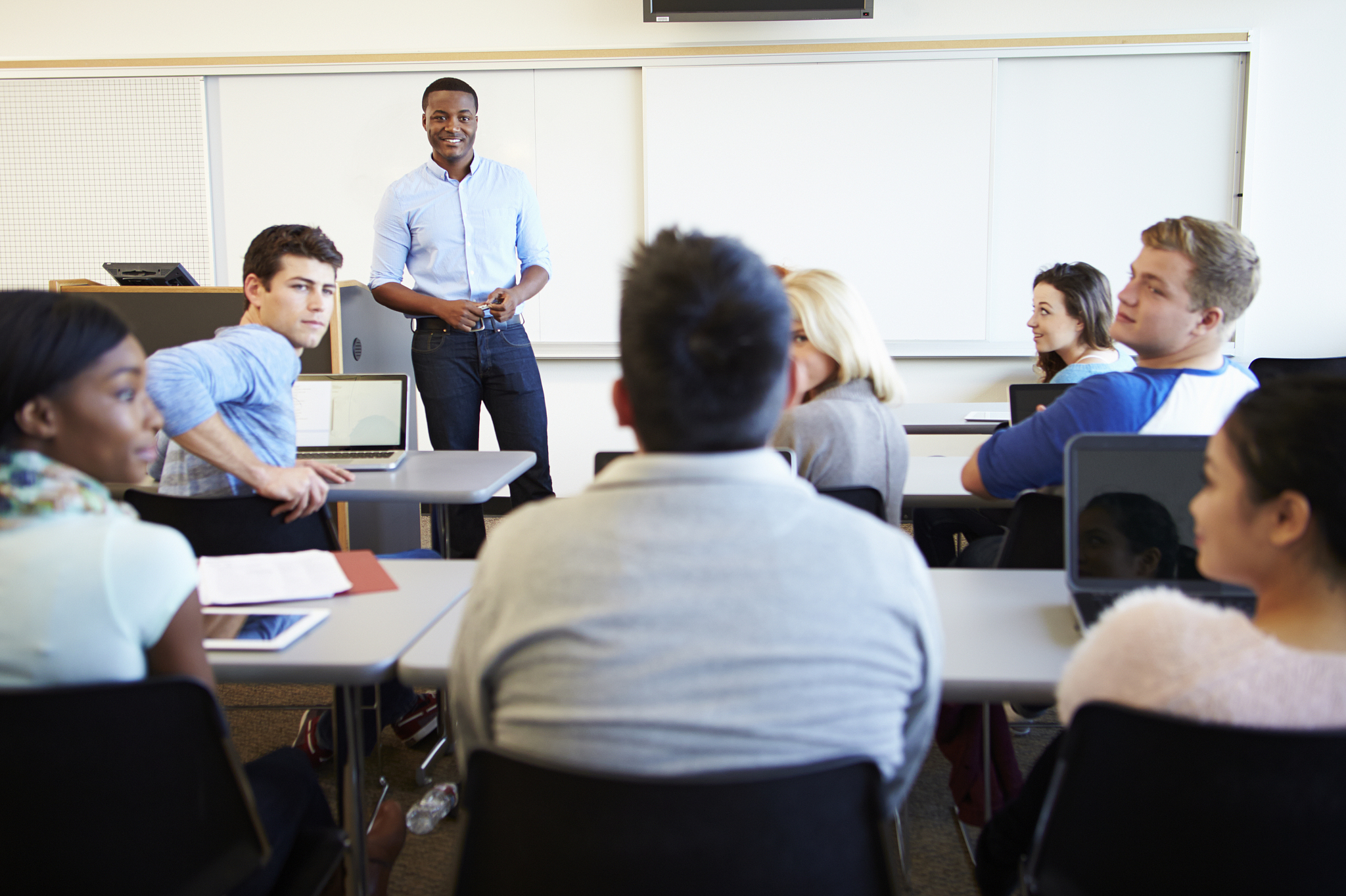 male tutor teaching university students in classroom