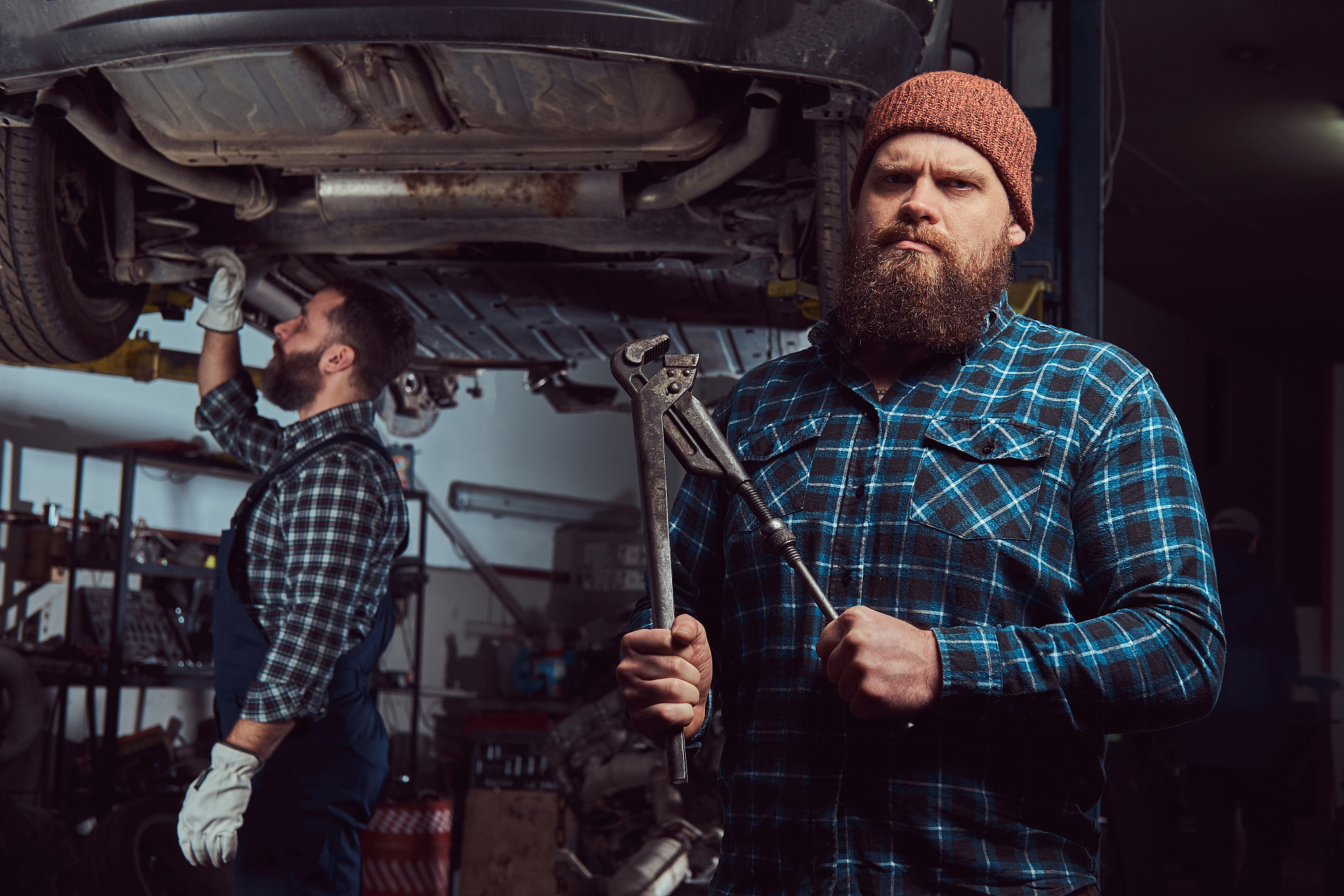 two bearded brutal mechanics repair a car on a lift in a garage.