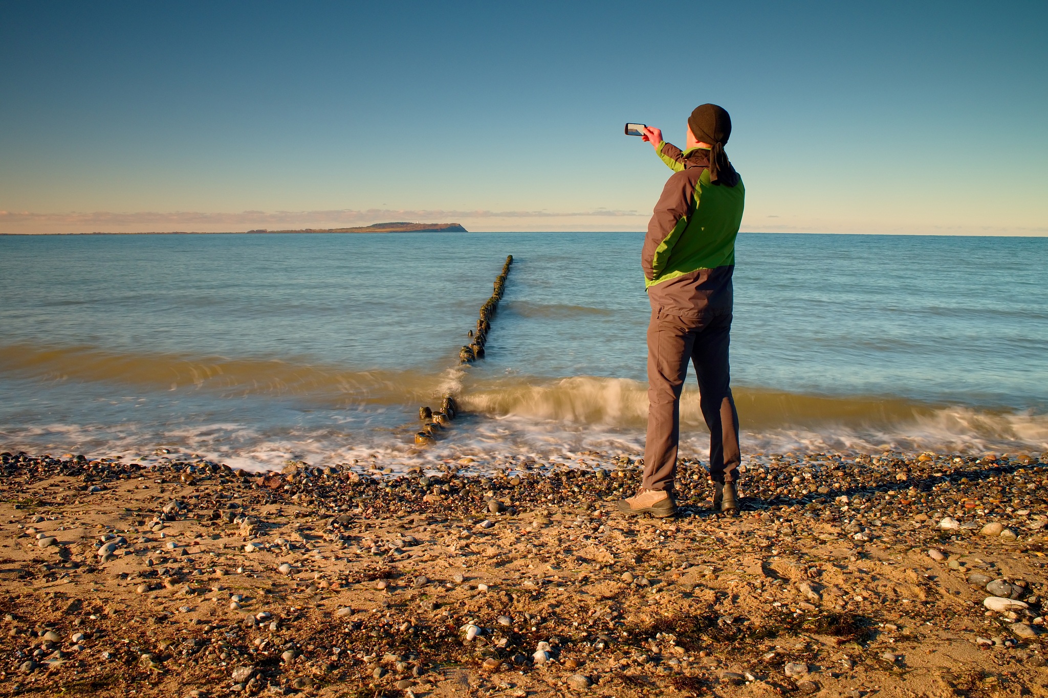 tourist hold cellphone, take picture of sea scenery at breakwate