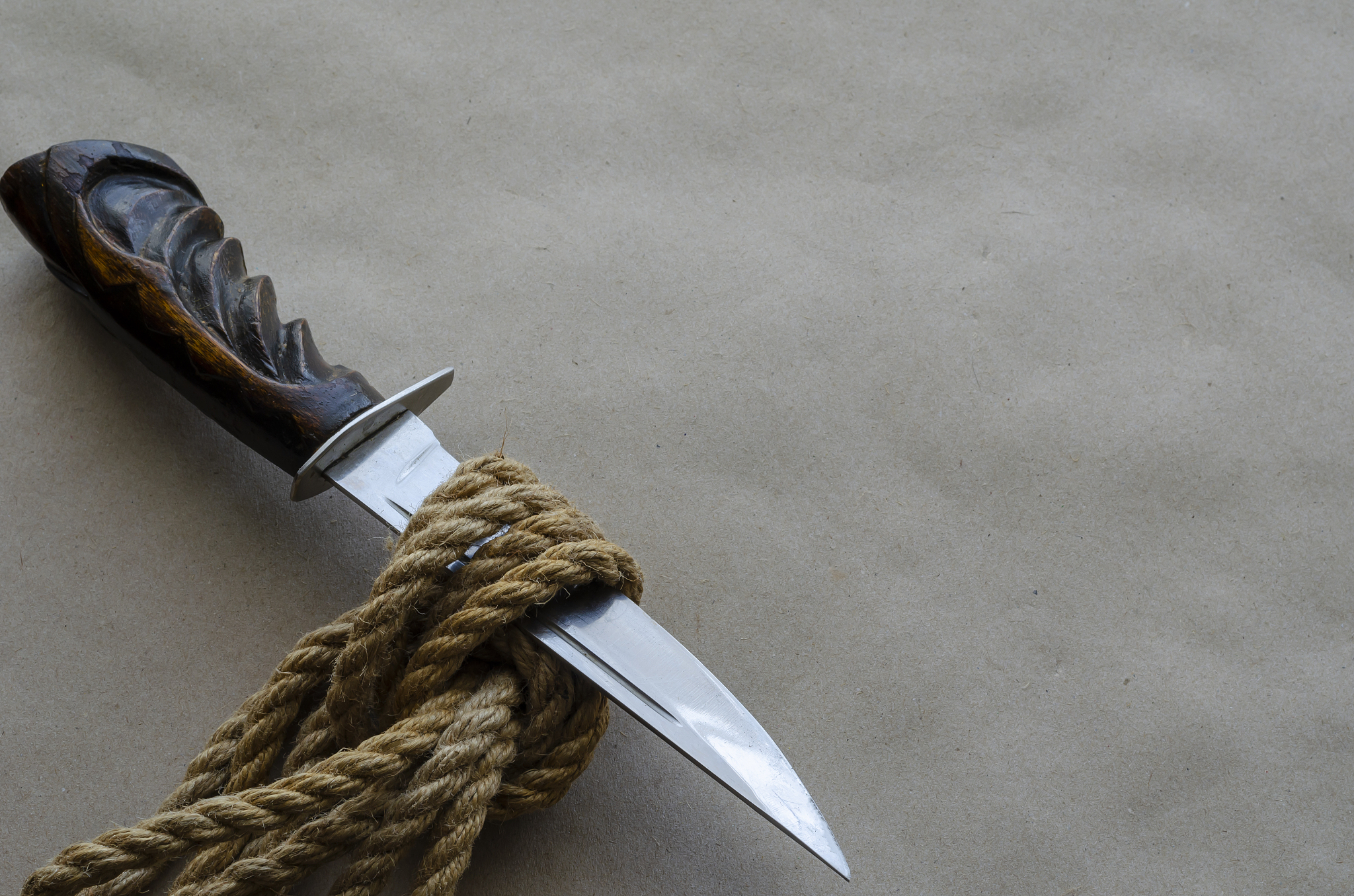 large knife with a wooden handle is stuck in a hemp rope knot.