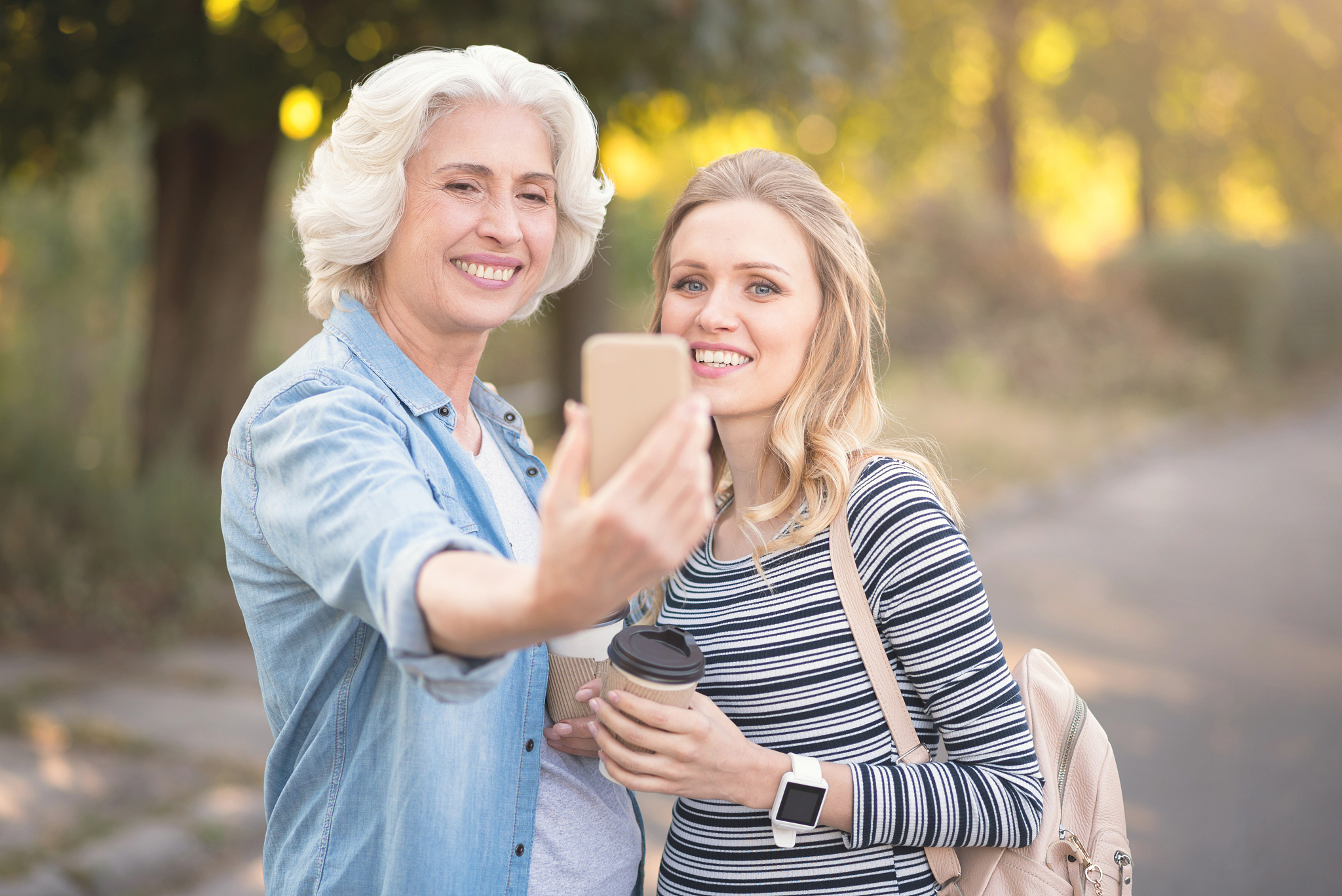 retired woman using gadget with pregnant daughter outdoors