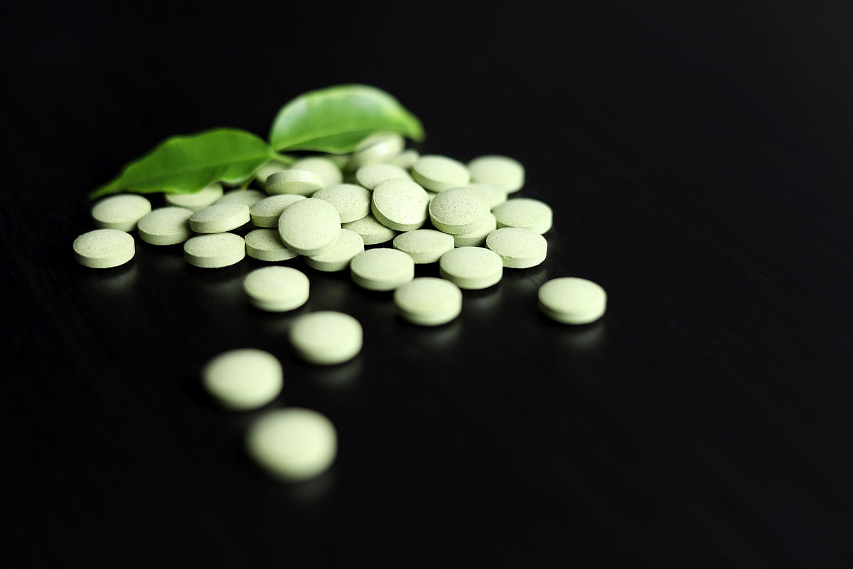 绿色药丸,叶子散落在深色的木桌上