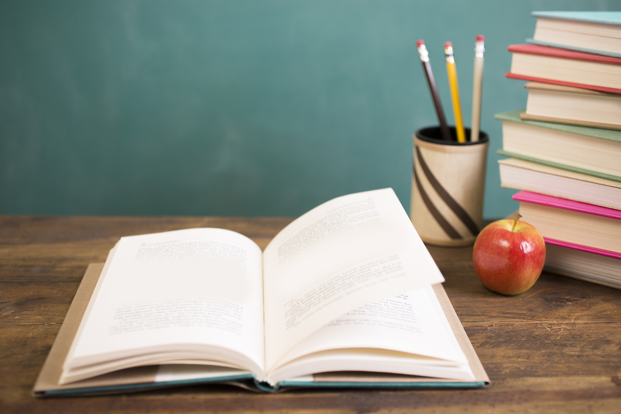 open book on school desk with pencils, apple and chalkboard.