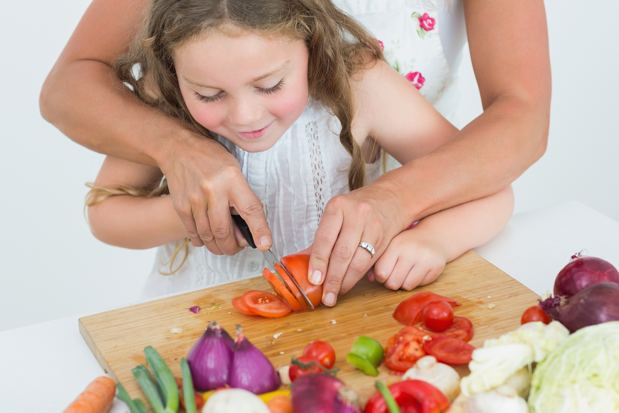 mother helping her smiling daughter to cut tomato