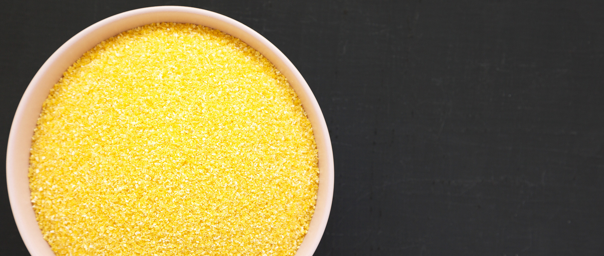dry organic masarepa corn meal in a pink bowl over black backgro