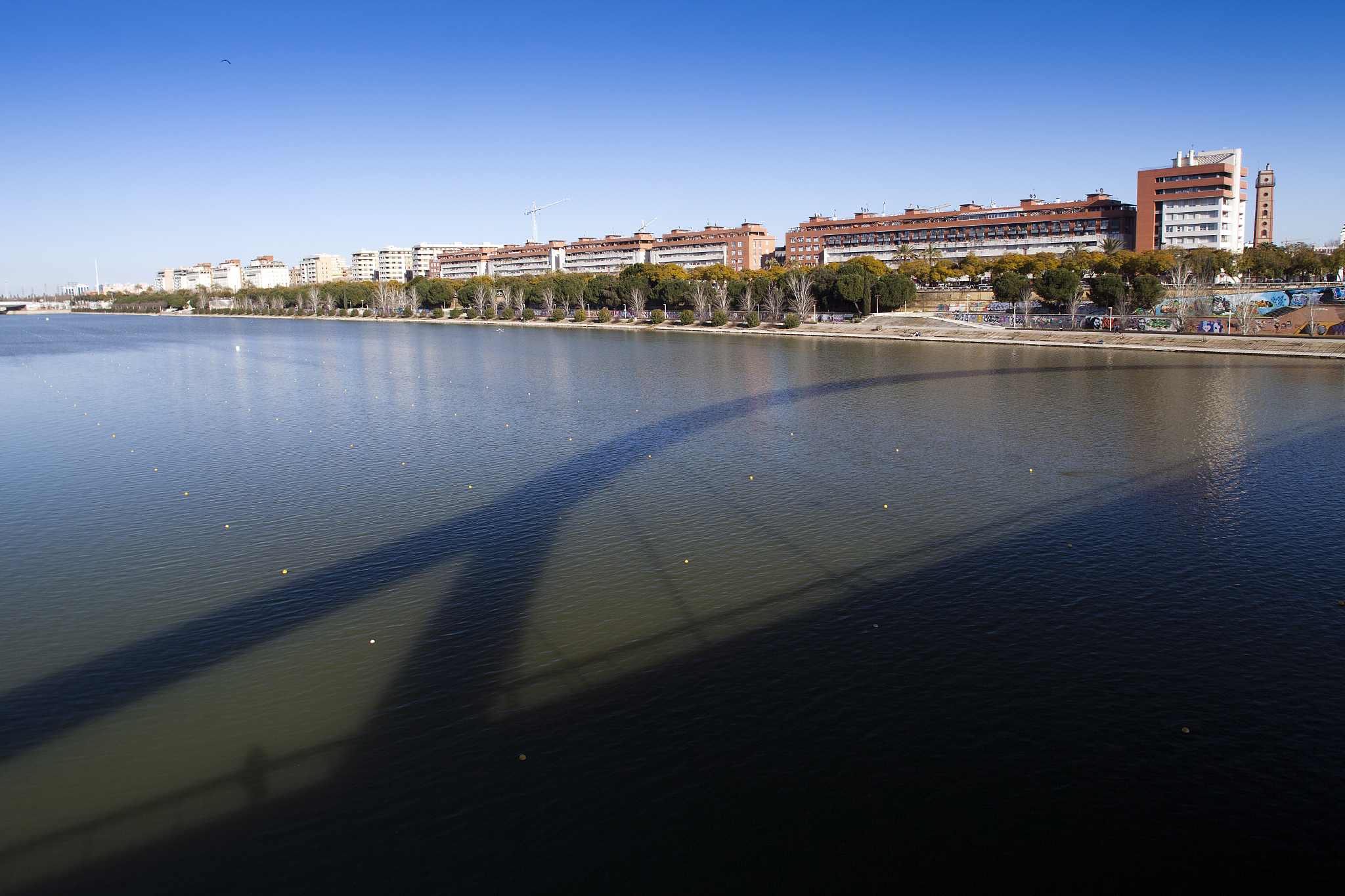 guadalquivir river from barqueta bridge, which casts its shadow 