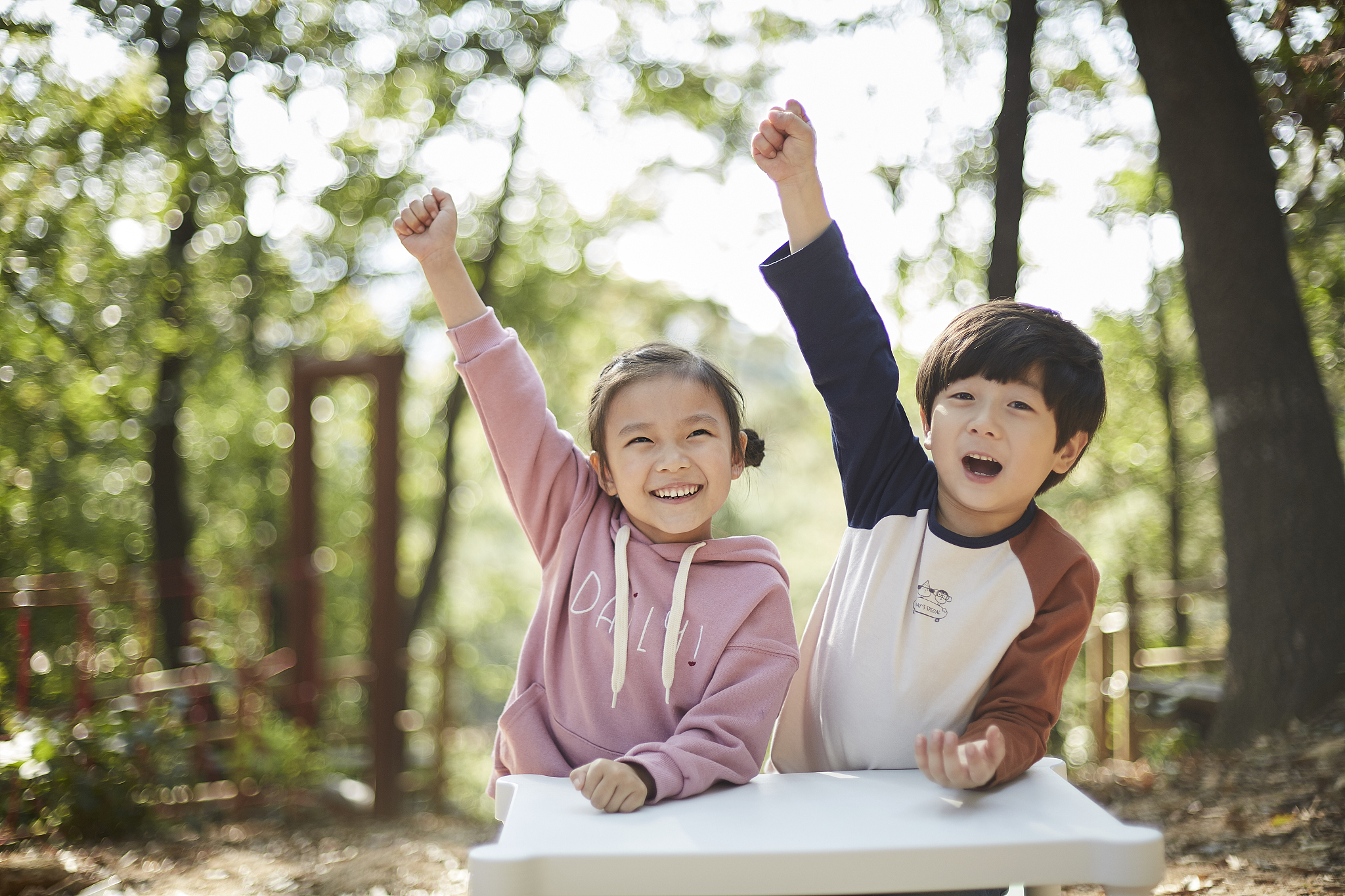 photography of little boy and girl raising hands sitting in fron