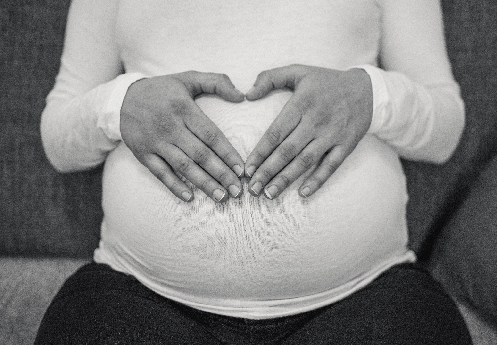 woman making a heart shape on her pregnant belly