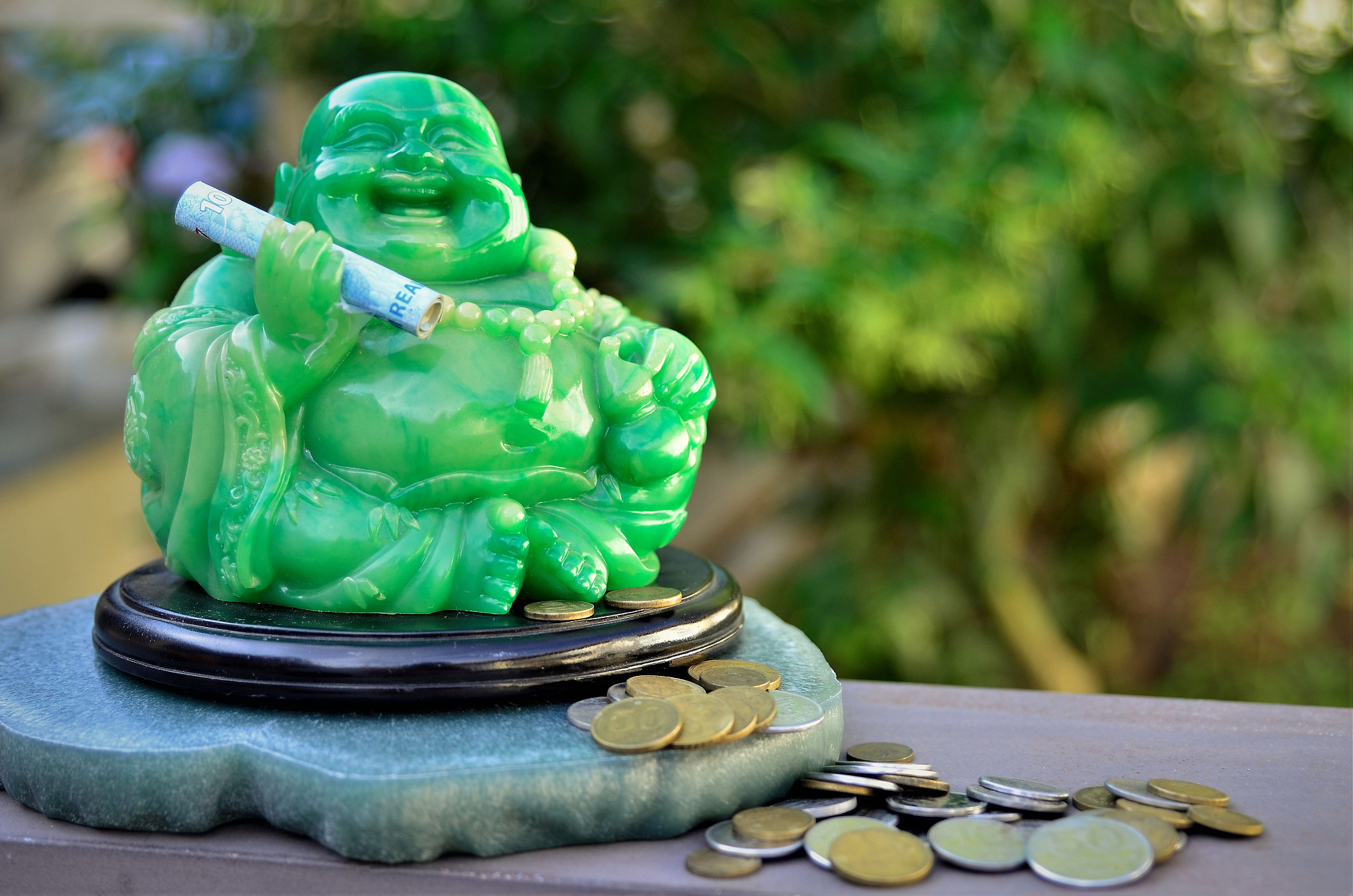 smiling green buddha with money in one hand and coins at his fee