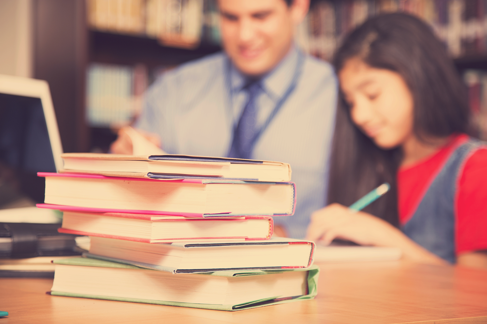 teacher, mentor helps elementary-age schoolgirl with homework.