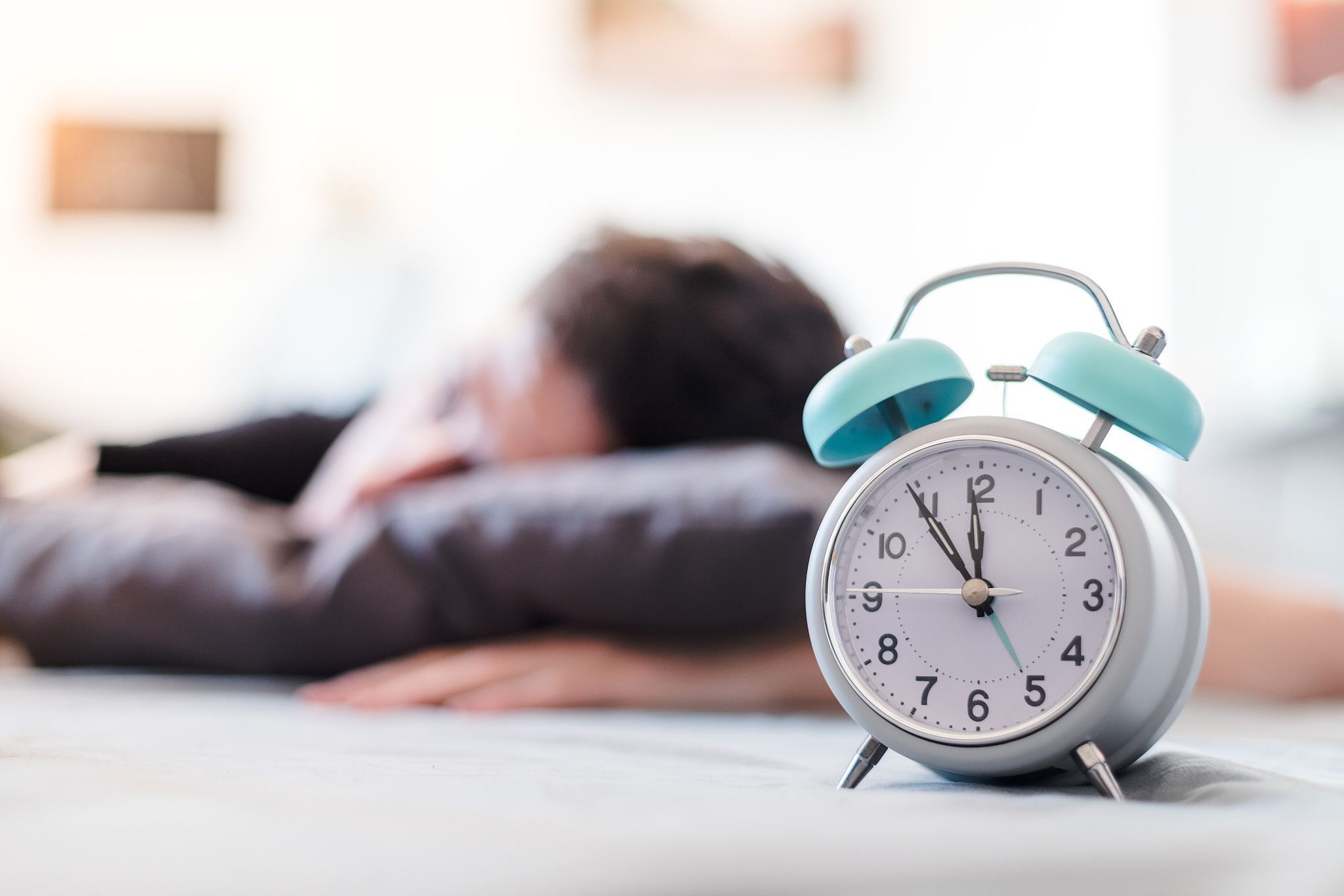 white alarm clock in the morning. young man sleeps in the backgr