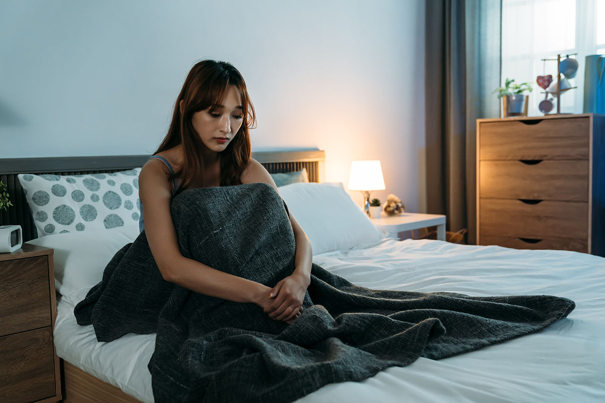 沮丧的亚洲女孩有失眠是坐在床上与她的手围绕膝盖感觉孤独在卧室黎明