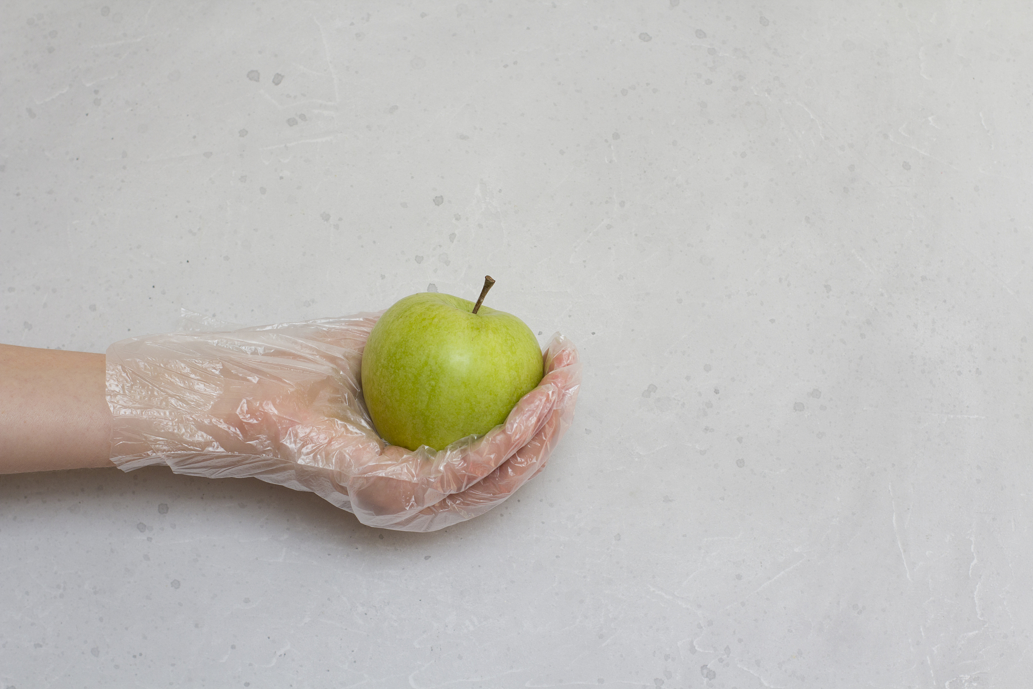 hand in disposable transparent glove holds green apple fruit. gr